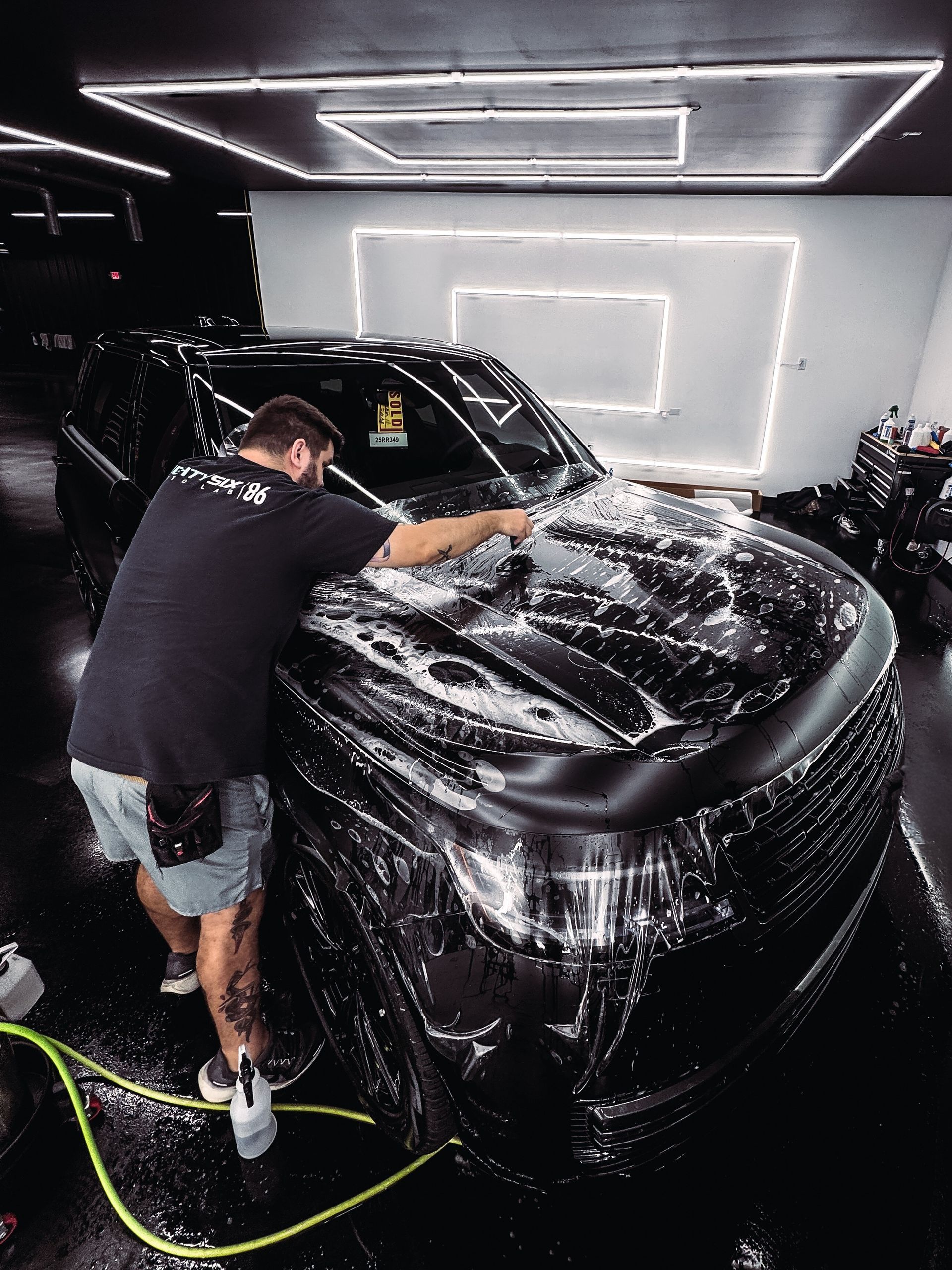 A person washing a black car with suds in a garage.