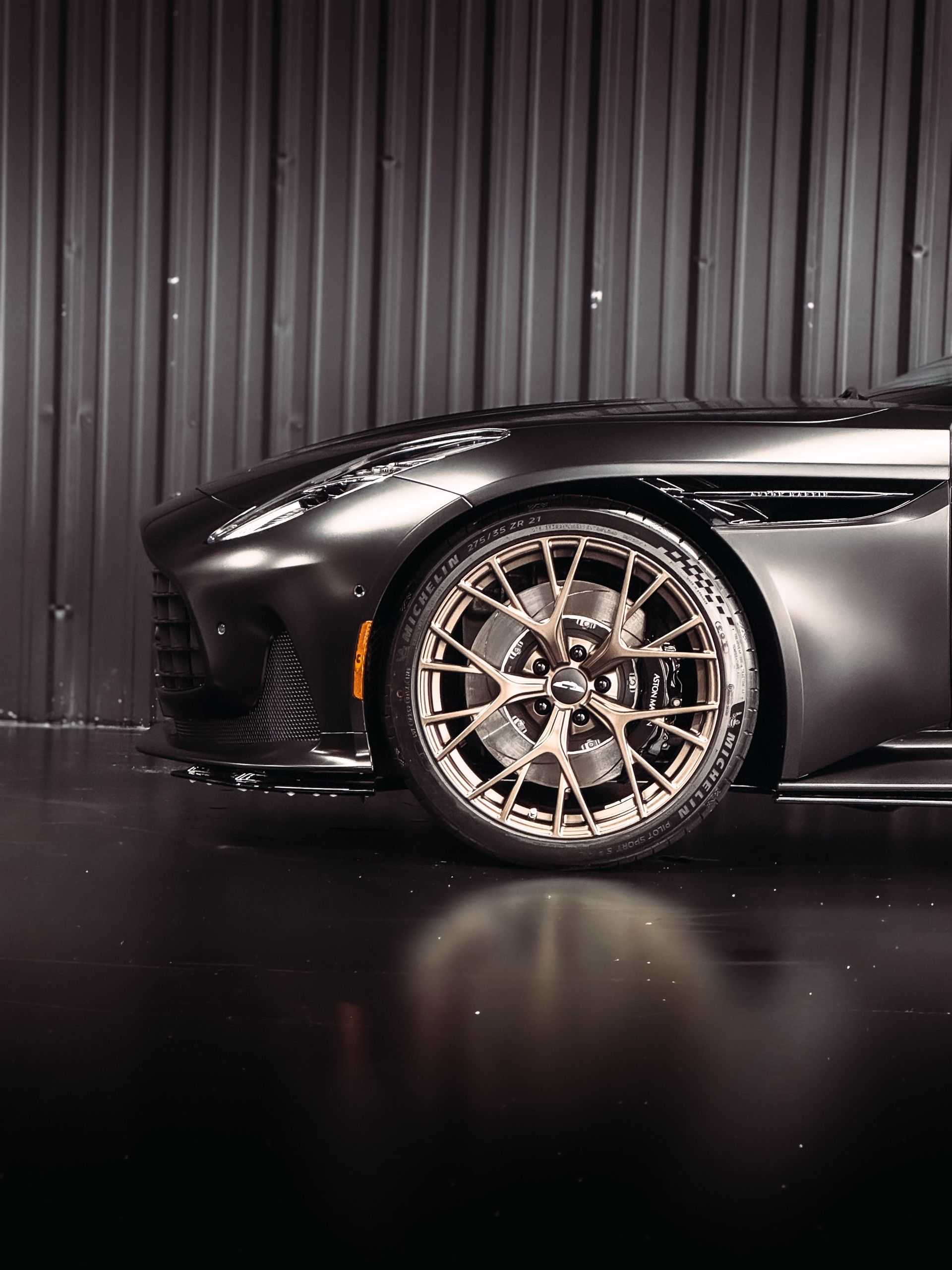 Black Aston Martin sports car, bronze rims, parked indoors, dark setting.