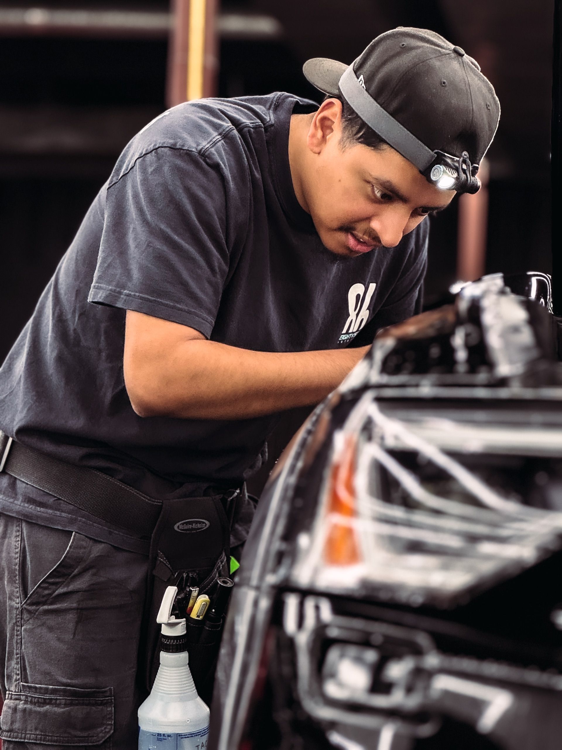 Man working on a car, wearing a headlamp. Leaning over the vehicle's engine compartment.
