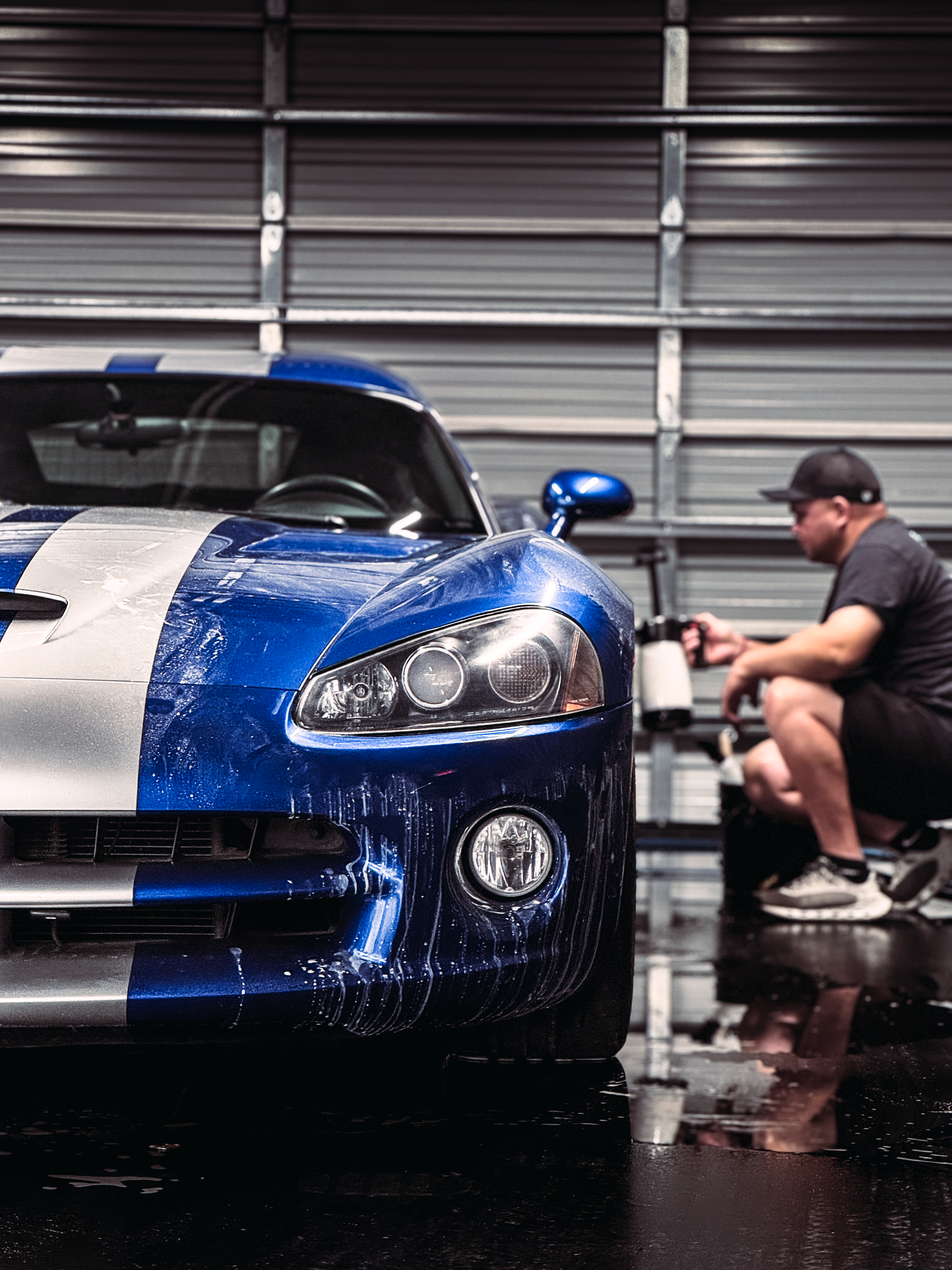 Blue and silver sports car being washed by a person in a garage.