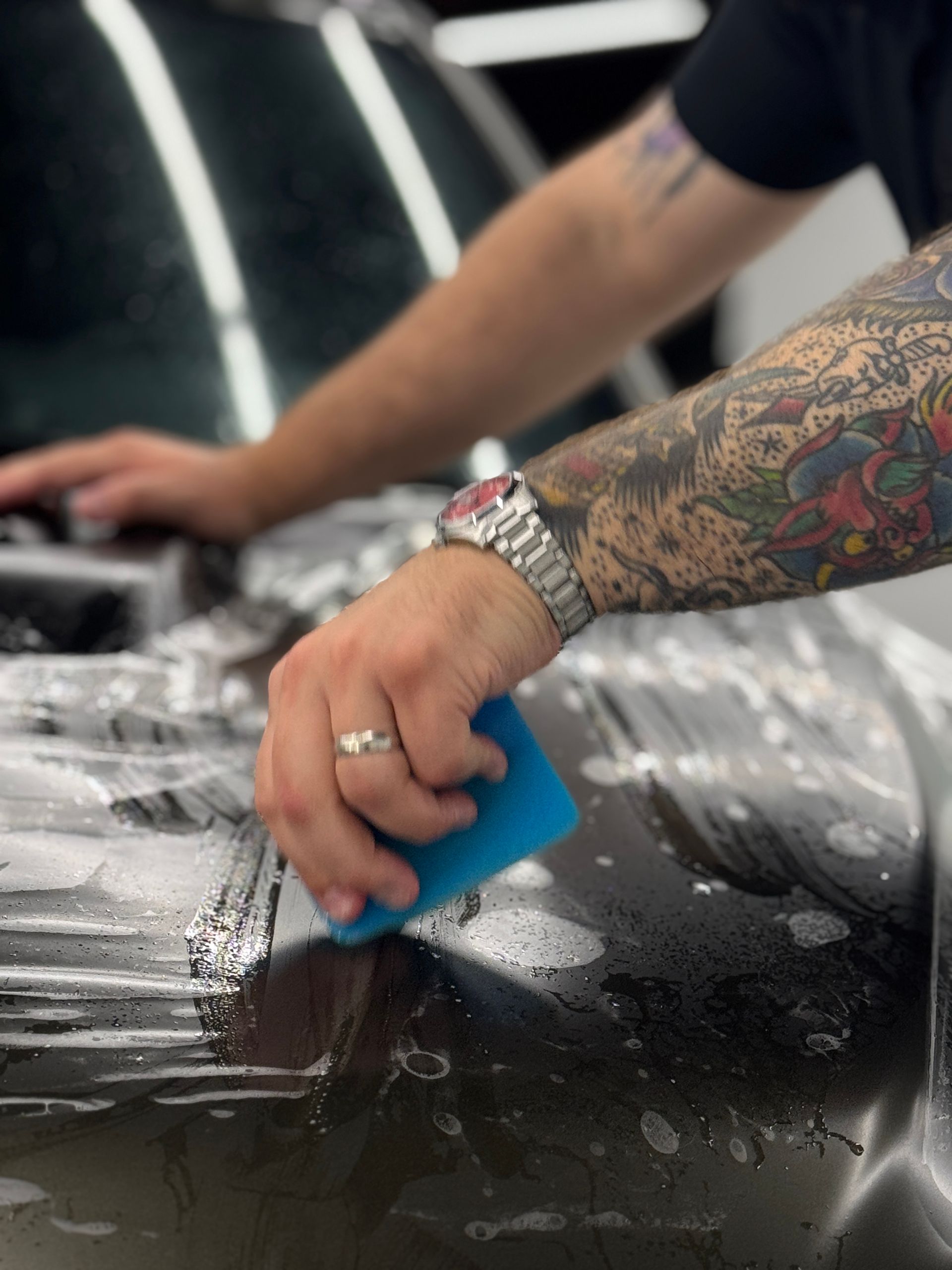 A person is applying a clear plastic covering to a car 's fender.