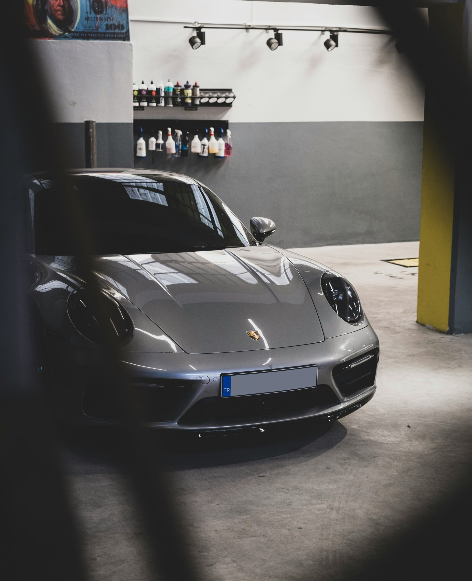 Silver Porsche in a garage with detailing products on a shelf.