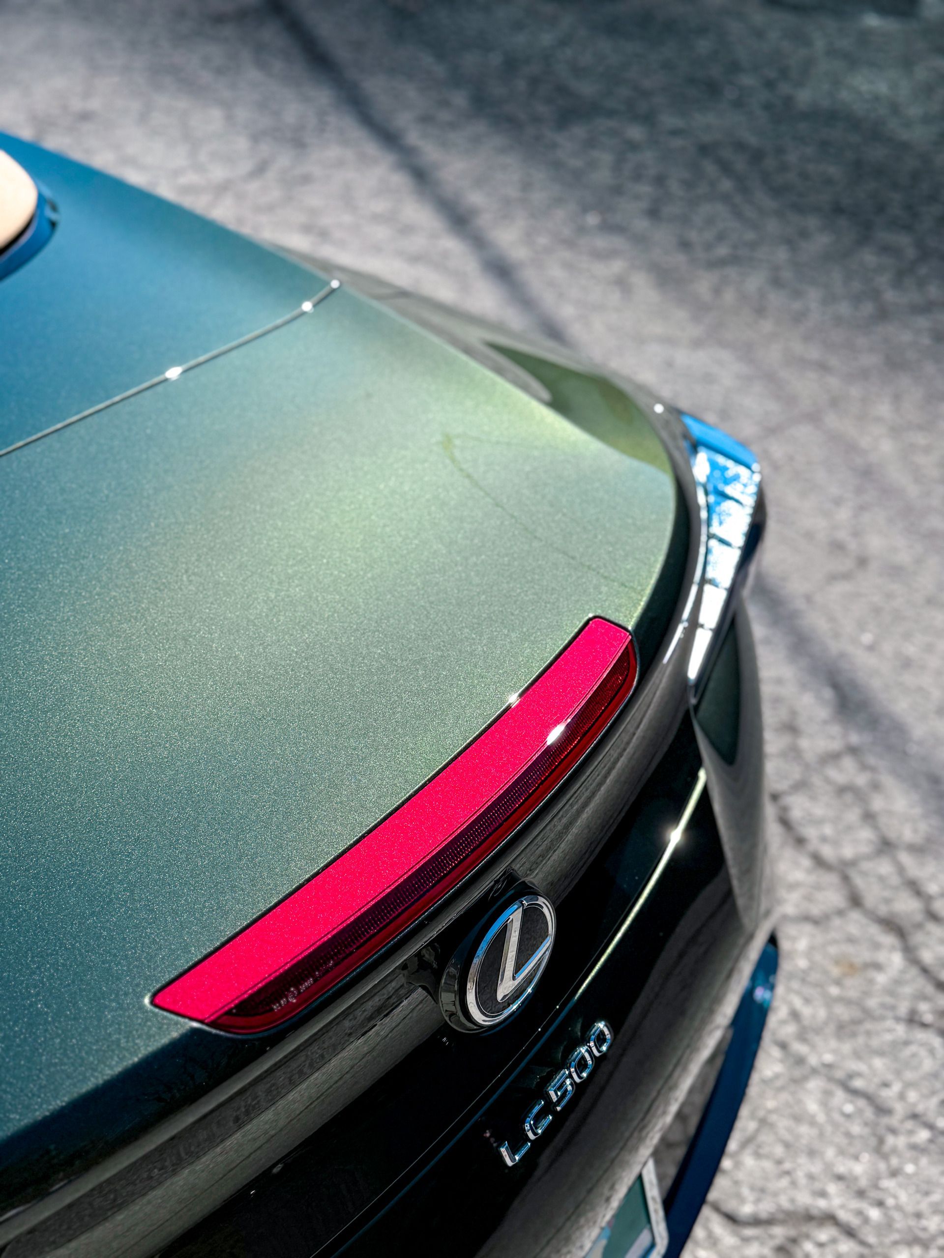 Rear view of a dark green Lexus L-600 with red brake light and chrome logo on asphalt.