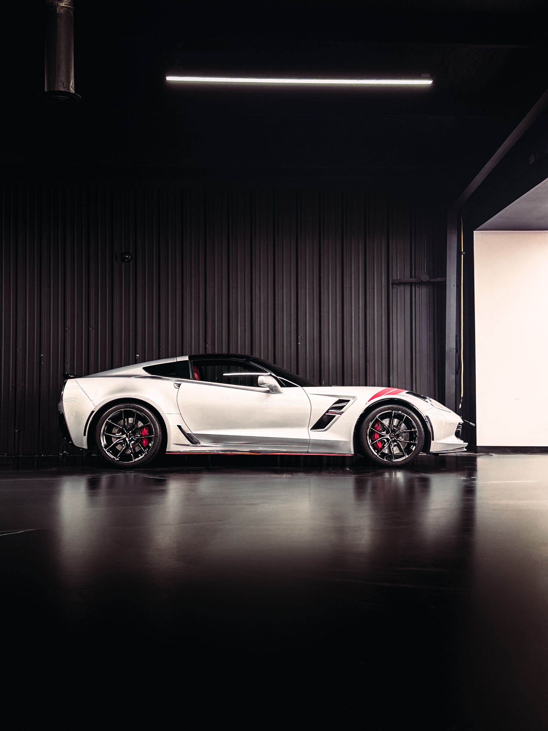 White Corvette sports car in a dark garage, black wheels, red accents.