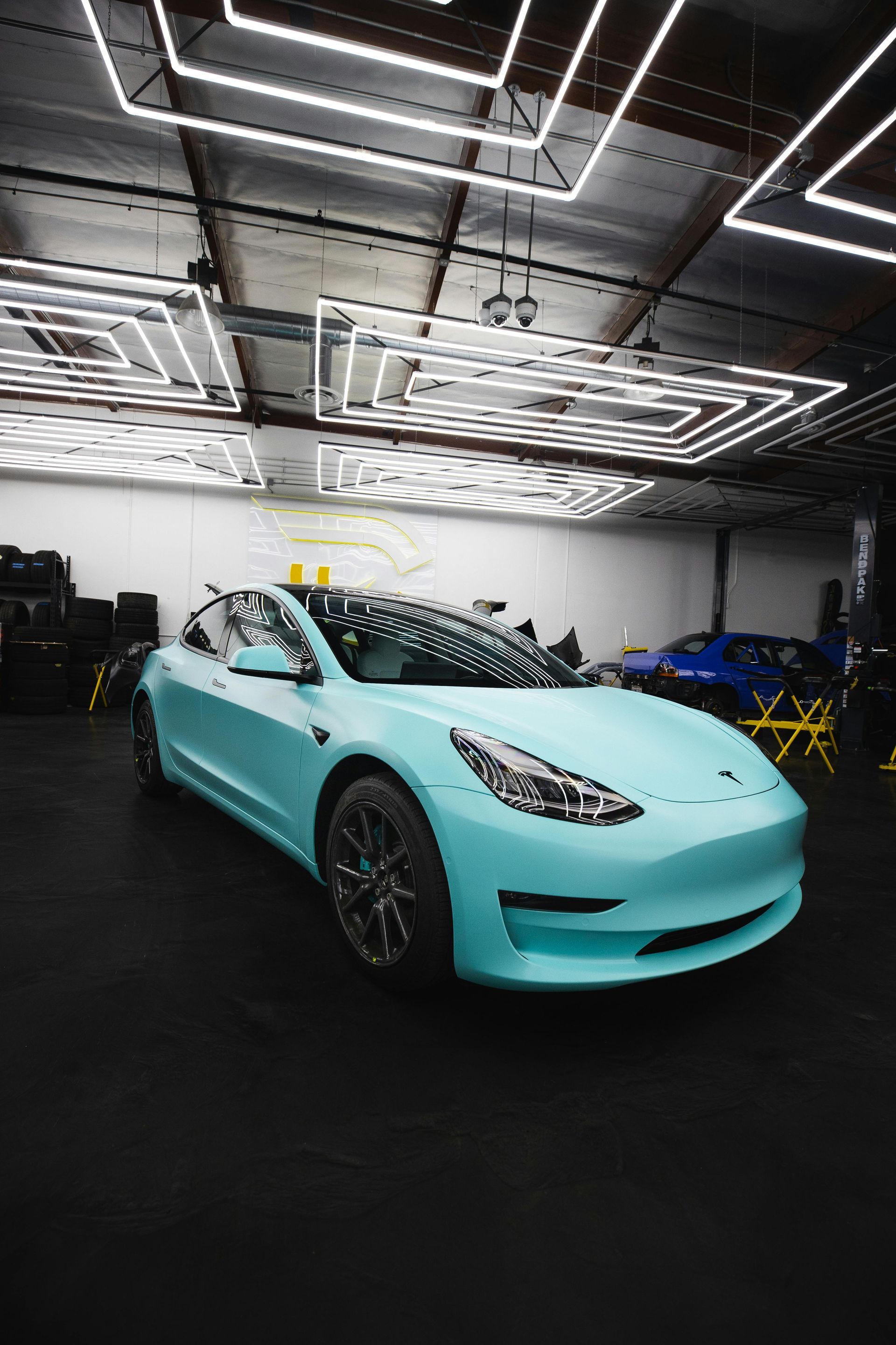 A blue tesla model 3 is parked in a garage.