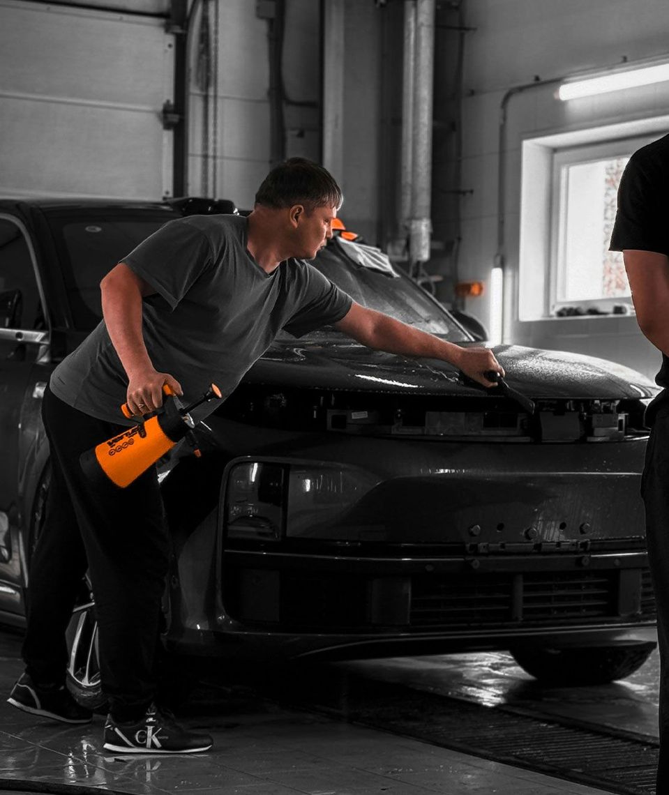 A man is cleaning a car with a spray bottle in a garage.