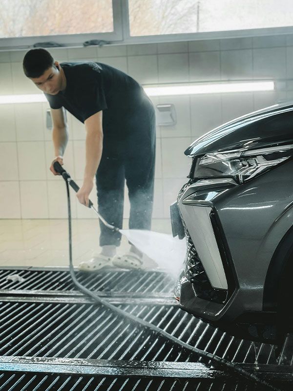 A man is washing a car with a hose in a car wash.