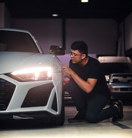 A man is kneeling next to a white car in a garage