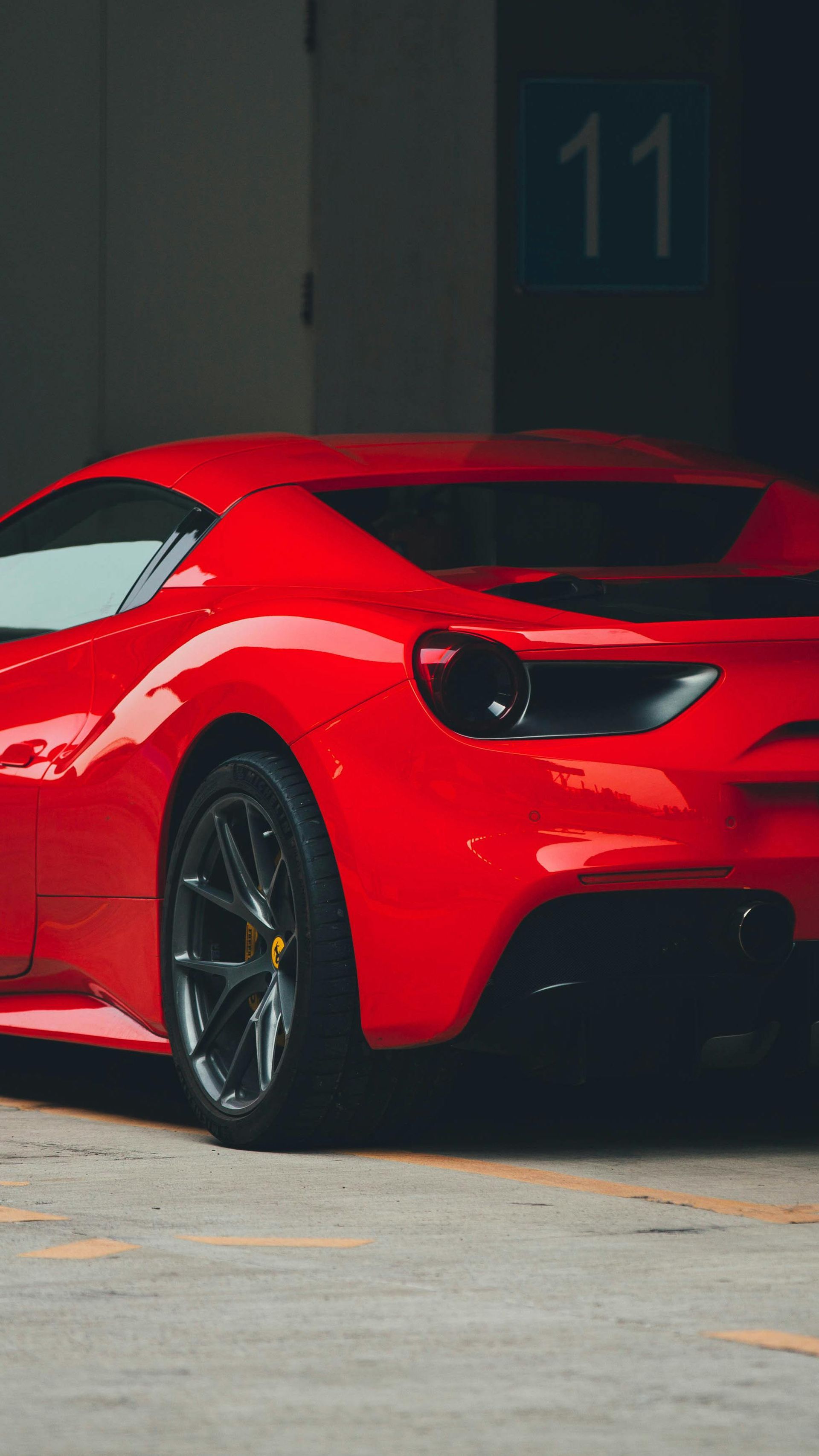 A red sports car is parked in a parking lot in front of a building with the number 11 on it.