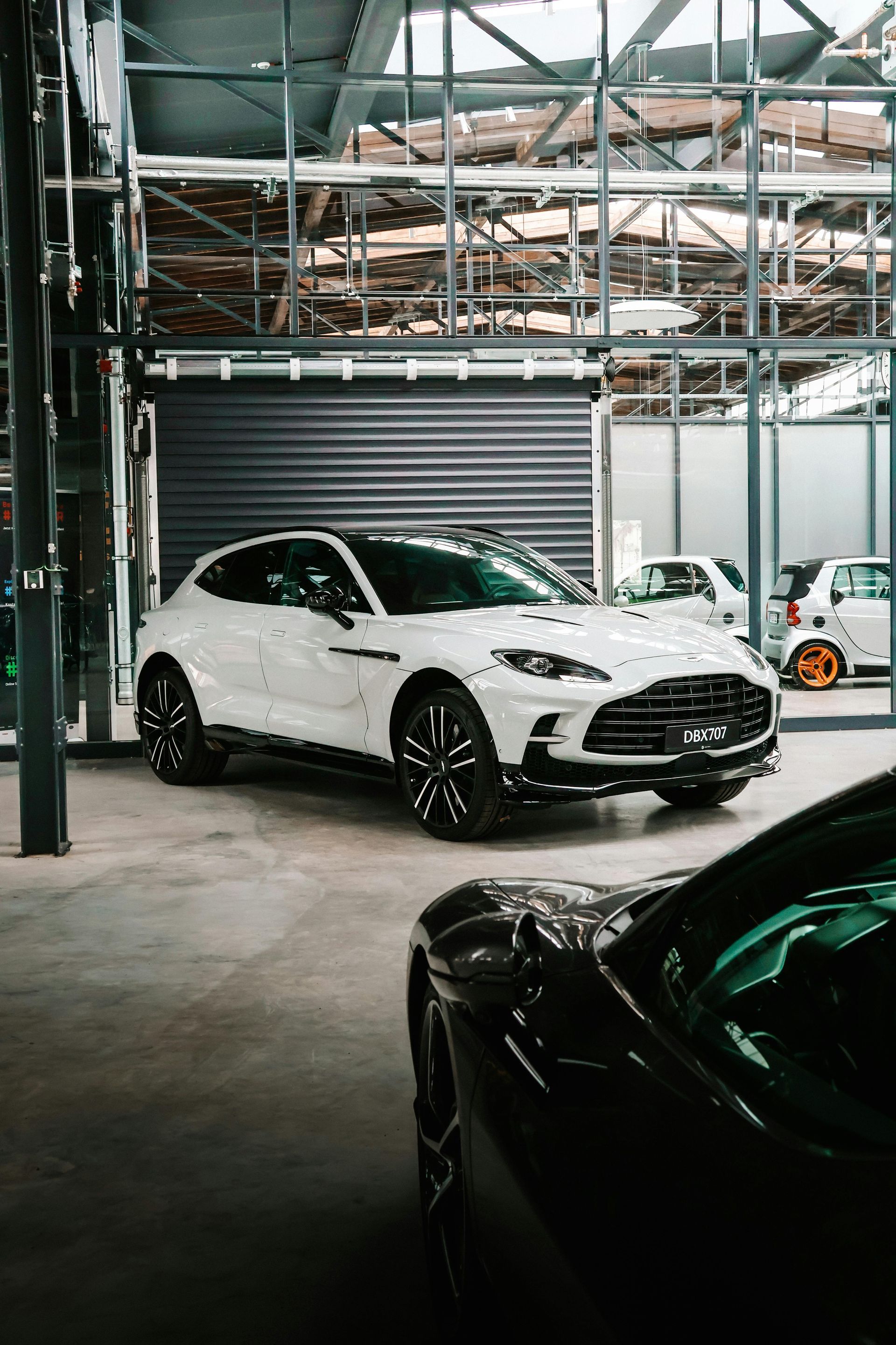 A white car is parked in a garage next to a black car.
