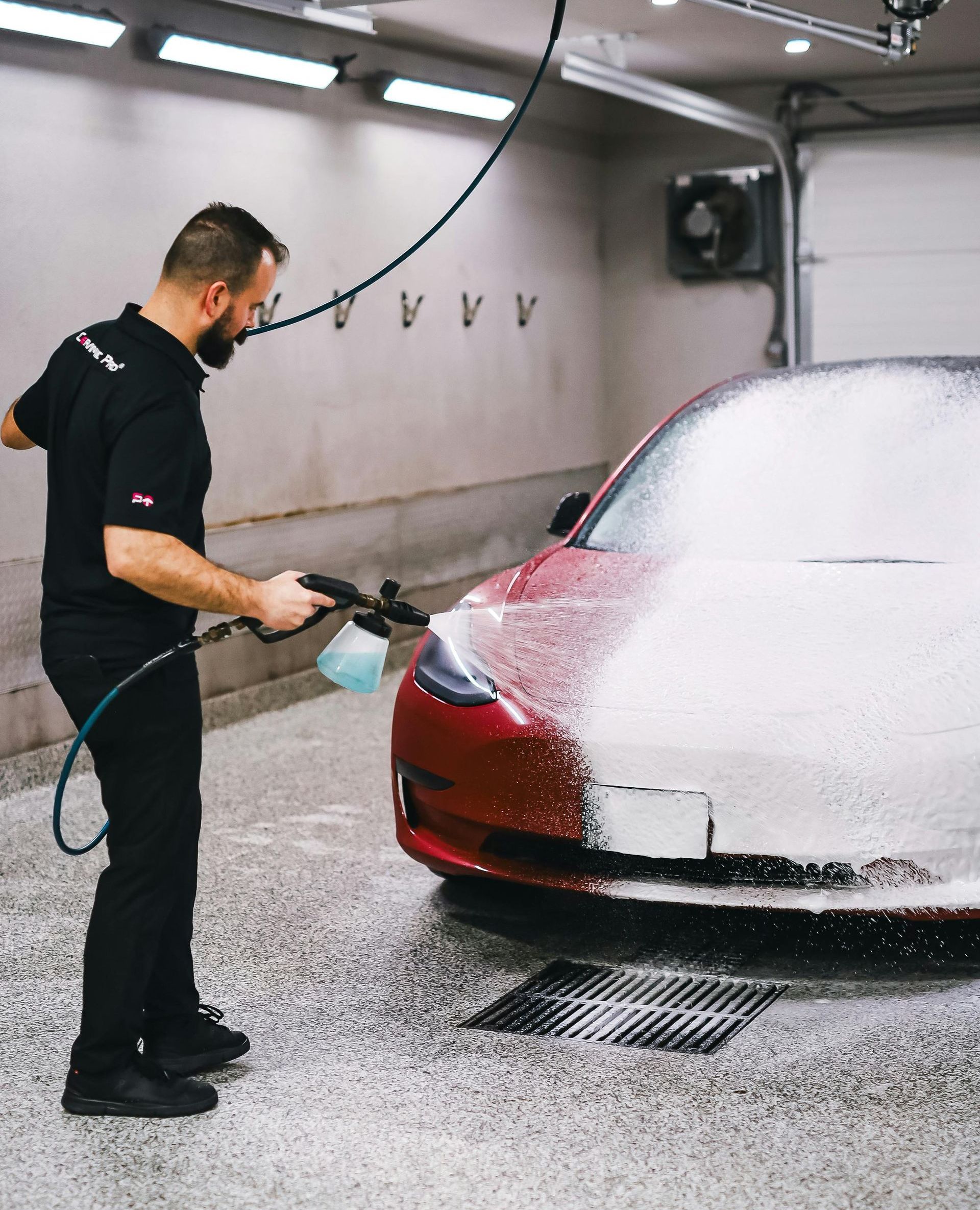 A man is washing a red tesla model 3 in a garage.