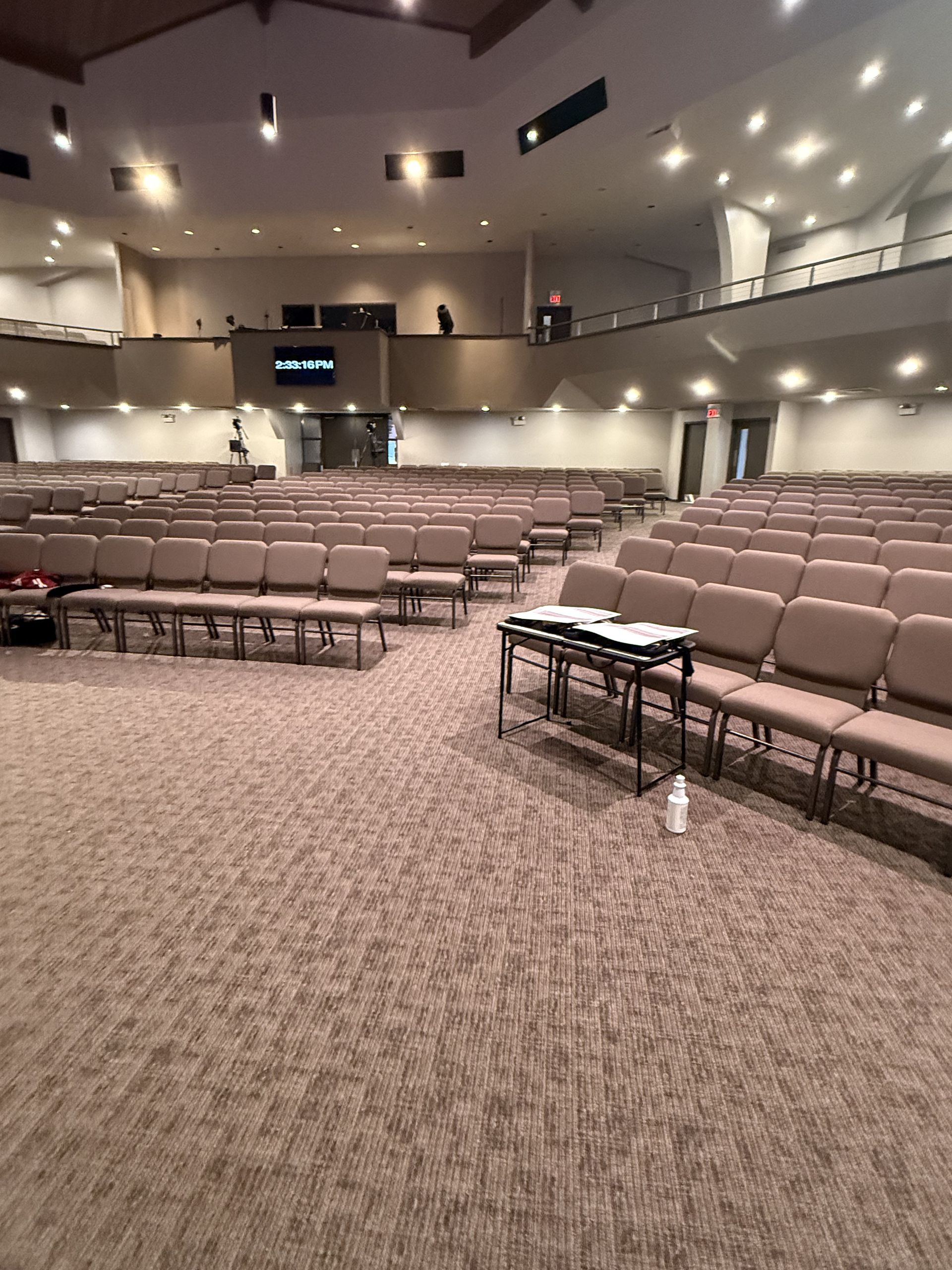 Empty auditorium with rows of beige seats and a carpeted stage area under soft ceiling lights