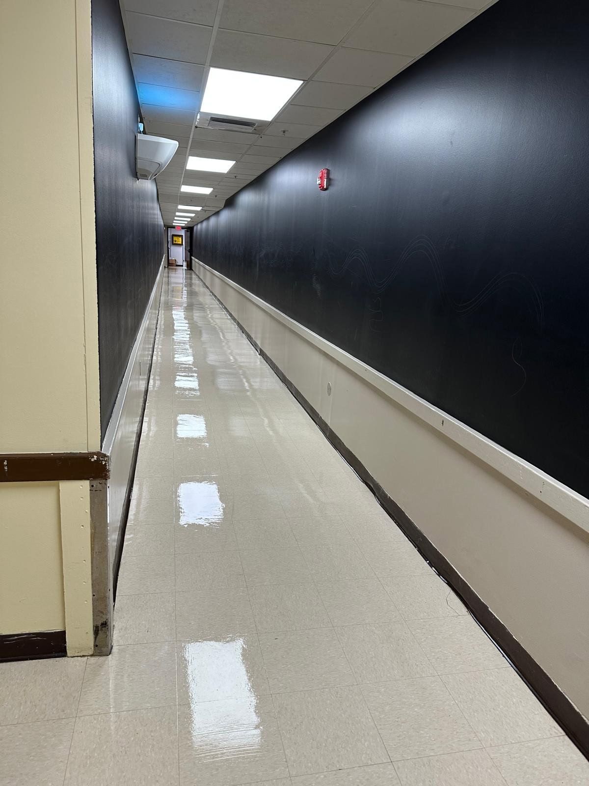 Long, empty hallway with dark walls, glossy floor, and fluorescent ceiling lights.