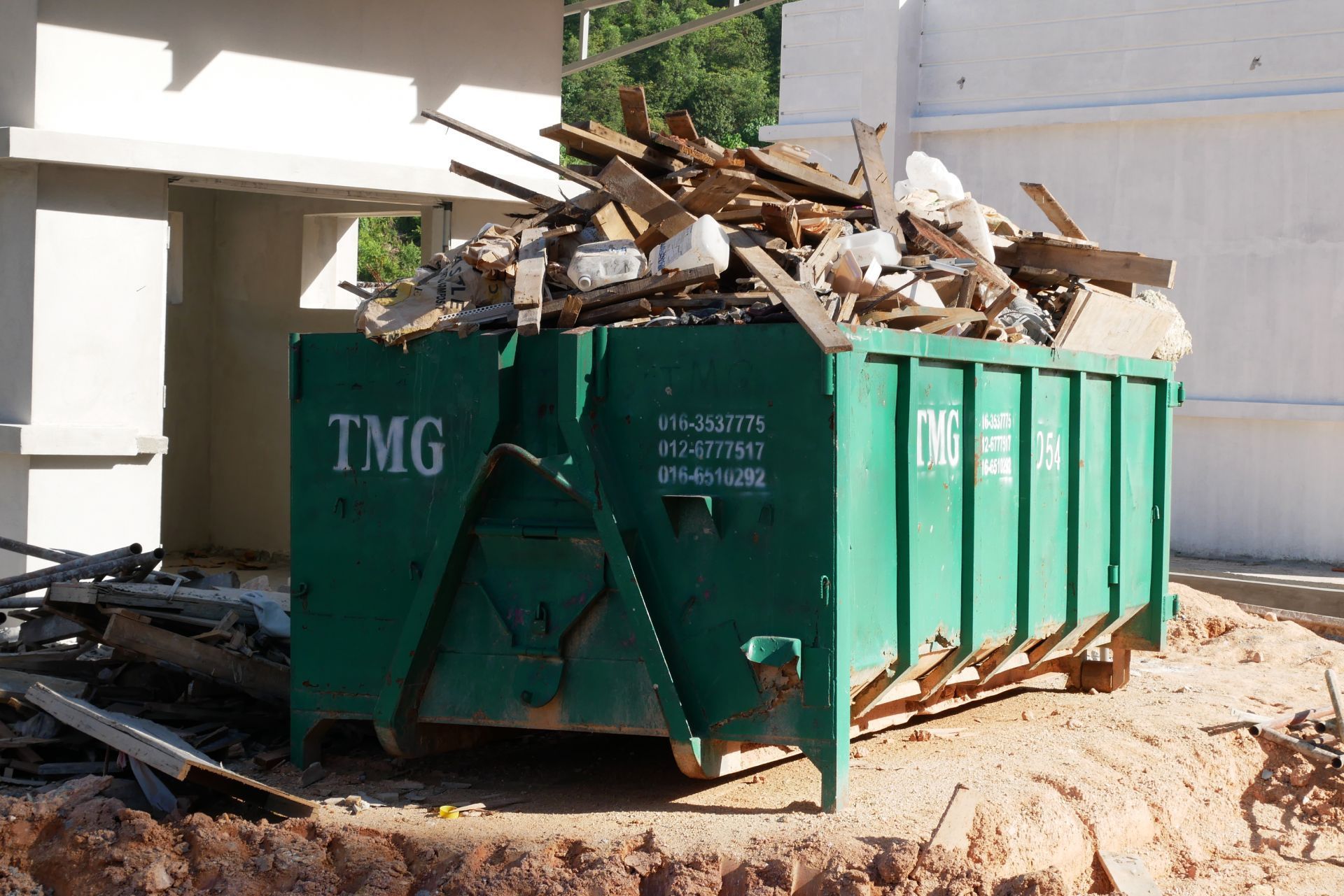 Green construction dumpster overflowing with wood debris beside a building site