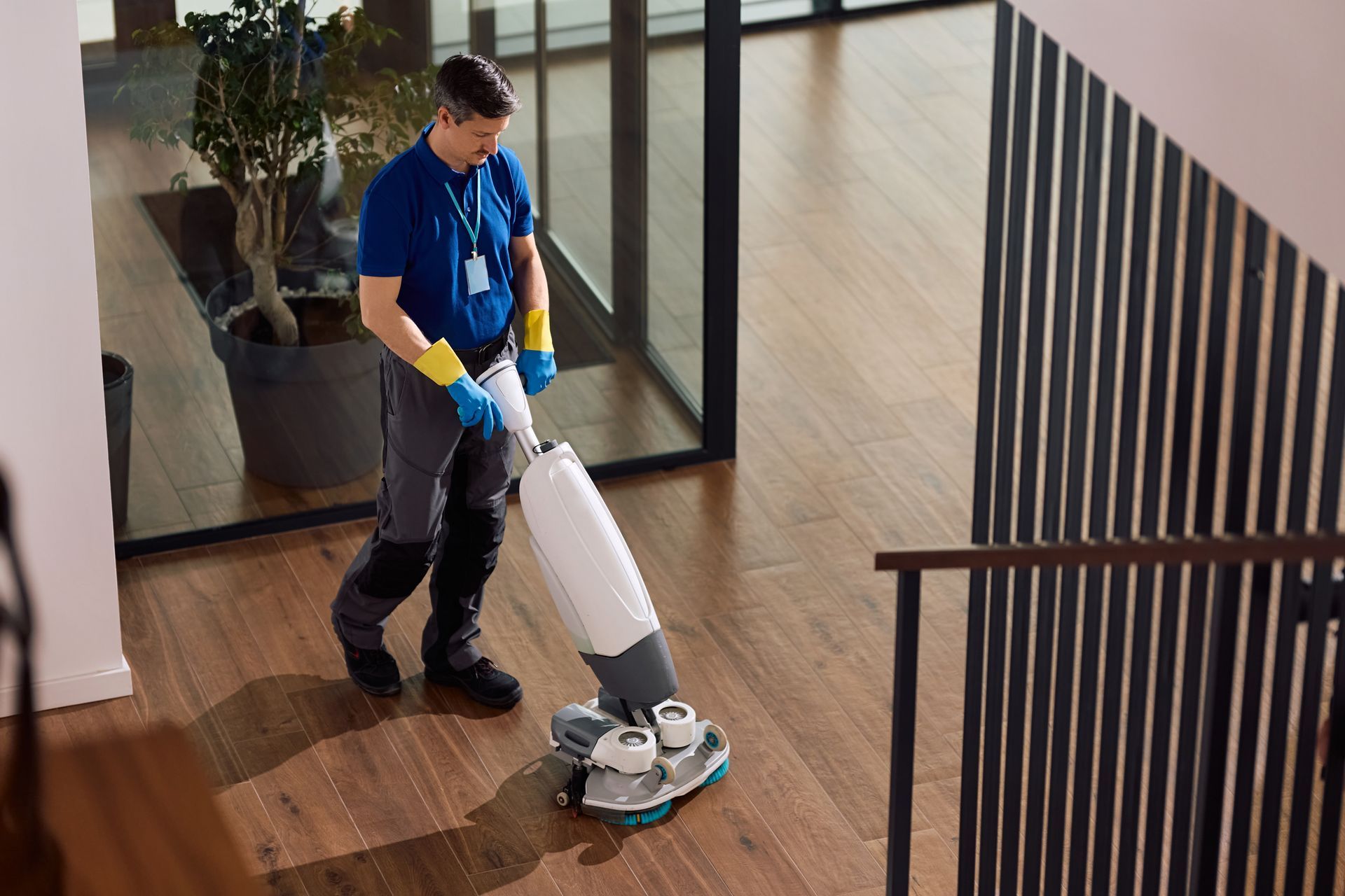 Person using a floor buffer on a wooden hallway floor indoors