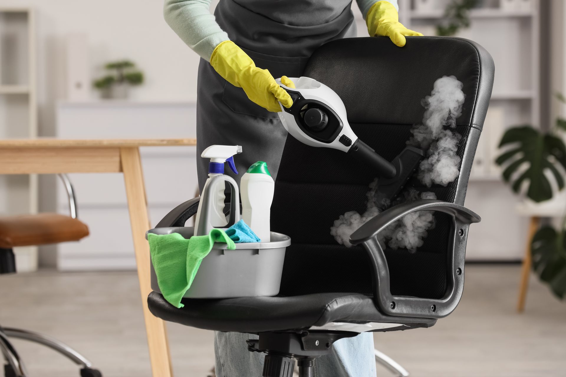 Person cleaning a black office chair with spray bottle and cloth in a bright room