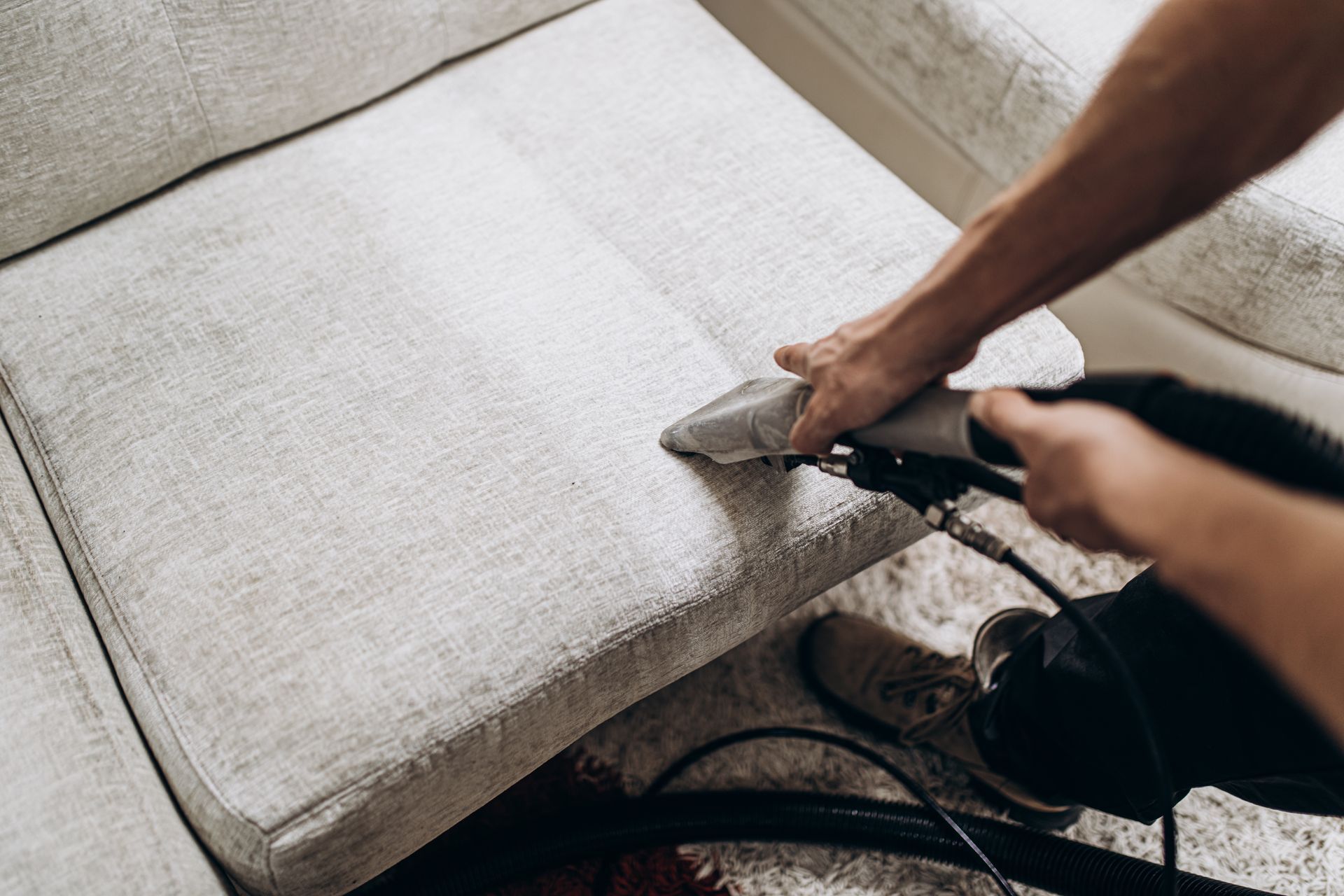 Hands steam-cleaning a white upholstered chair cushion.