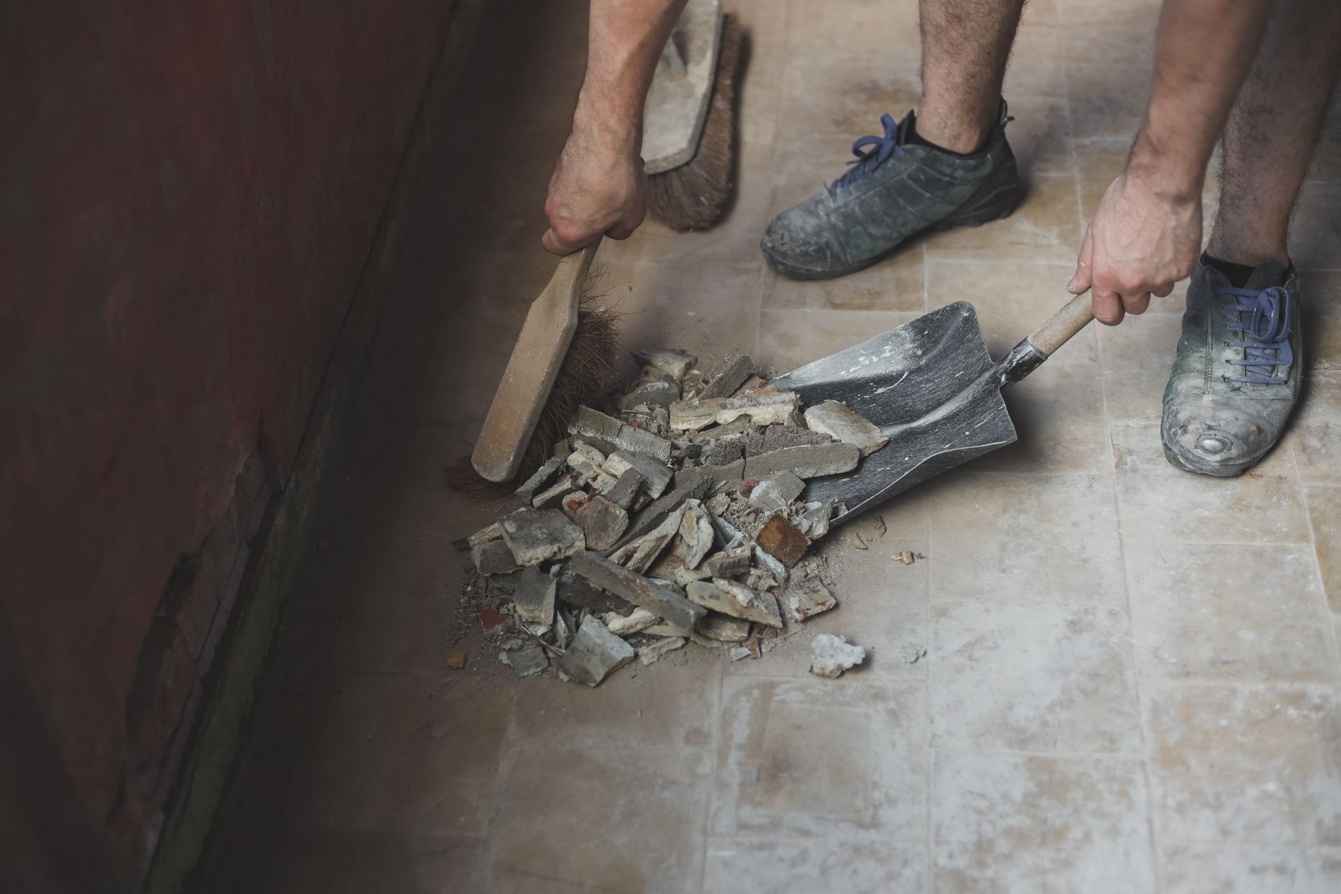 Two people using shovels to scoop rubble and debris from a dusty floor indoors