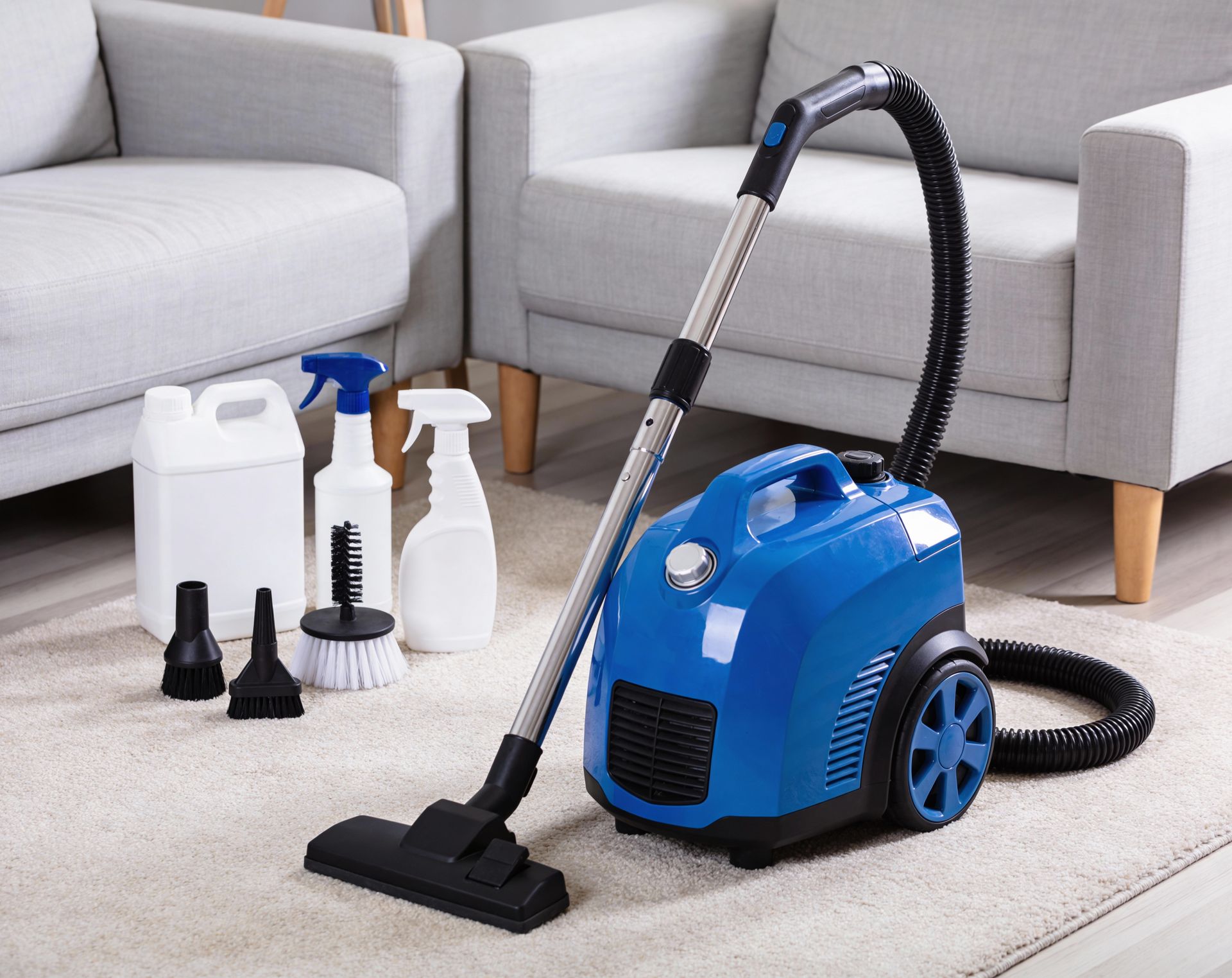 Blue canister vacuum cleaner with cleaning attachments on a carpeted floor in a living room