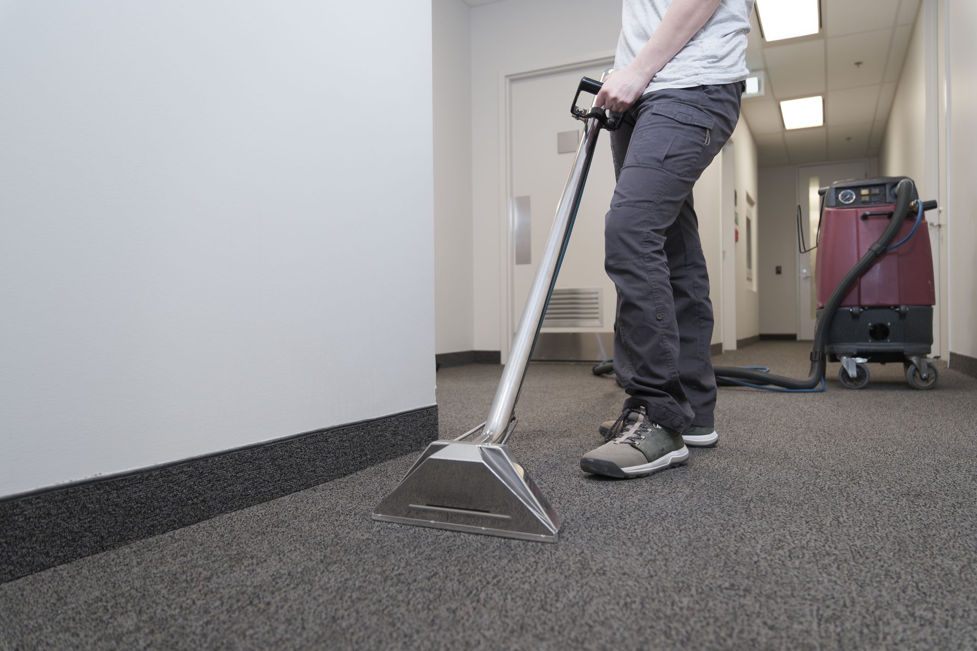 Person using a carpet cleaning machine in a hallway with gray carpet and white walls