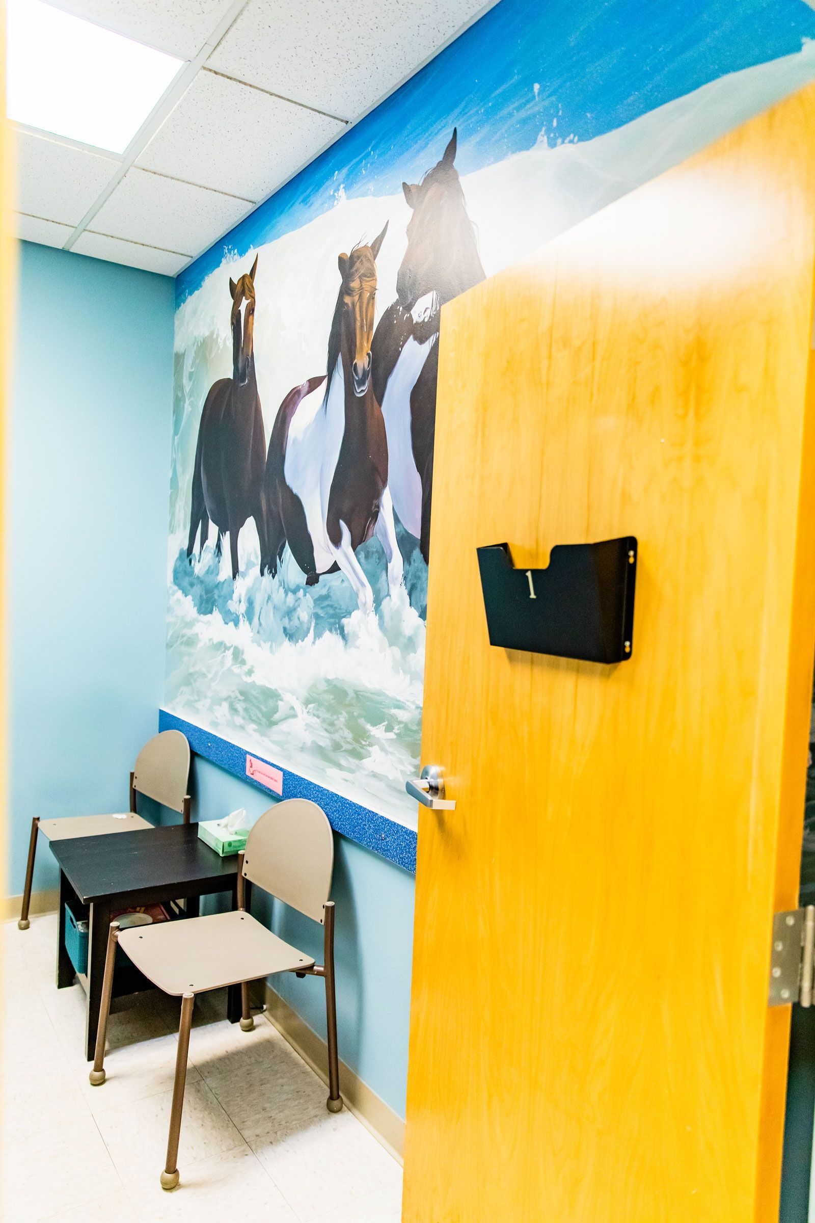 A waiting room with a mural of horses on the wall.
