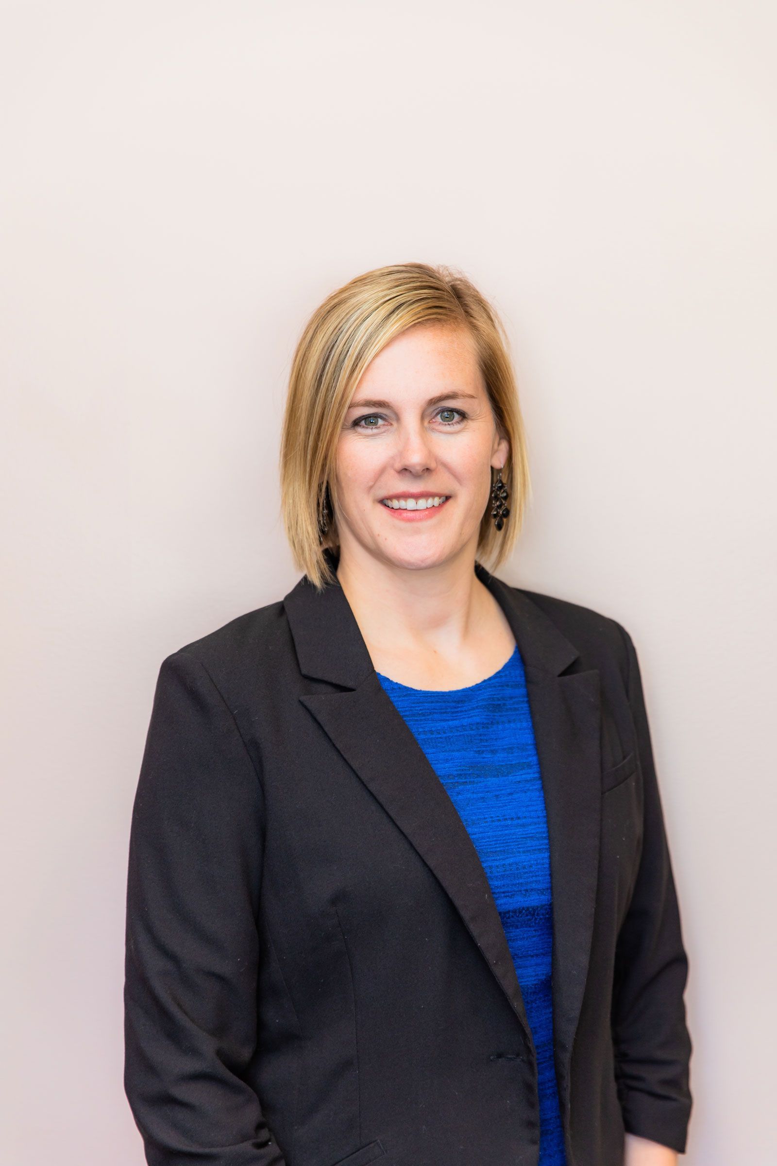 A woman in a black jacket and blue shirt is smiling for the camera.