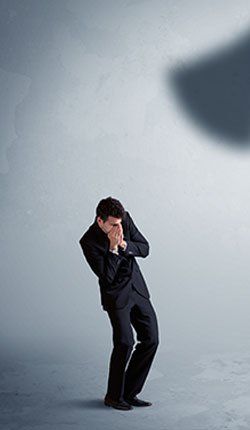 Un homme en costume se couvre le visage avec ses mains alors qu'il se tient devant un mur.