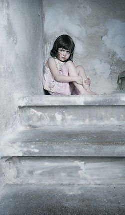 Une petite fille est assise sur les marches d'un immeuble.