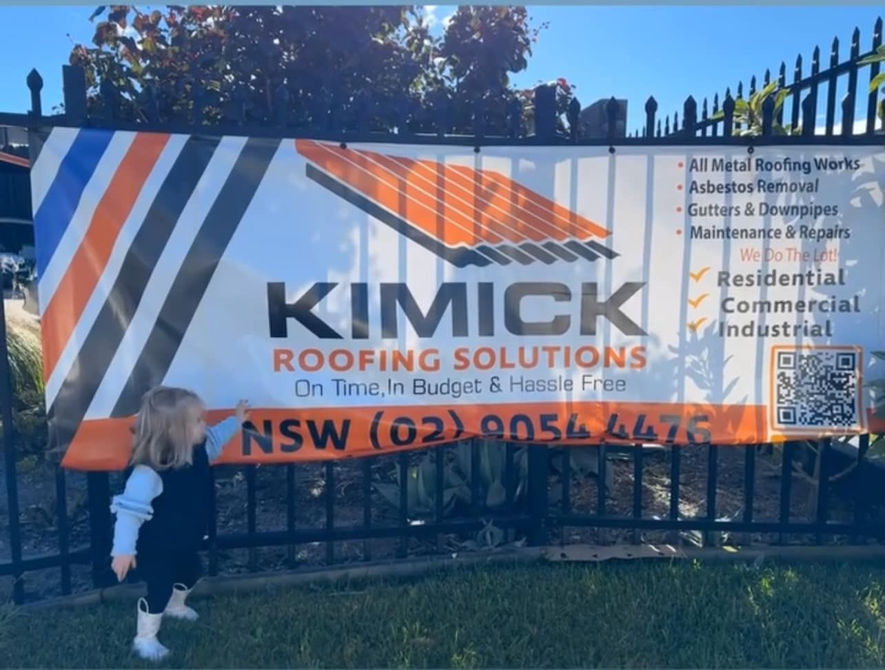 A Little Girl Standing In Front Of A Sign For Kimick Roofing Solutions — Kimick Roofing Solutions In Wyong, NSW