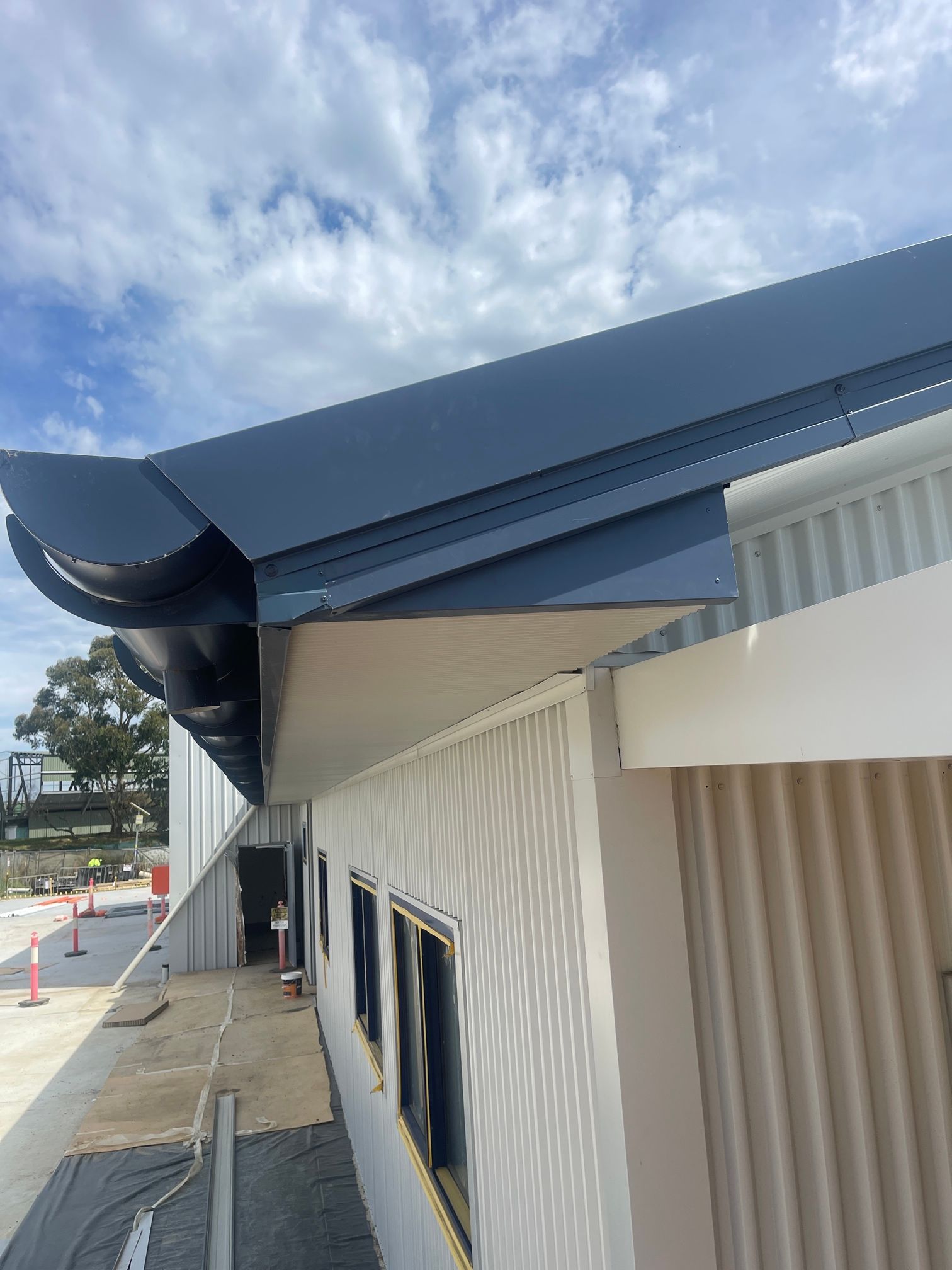 A Side Profile Of A Cream Building In A Construction Zone — Kimick Roofing Solutions In Wyong, NSW