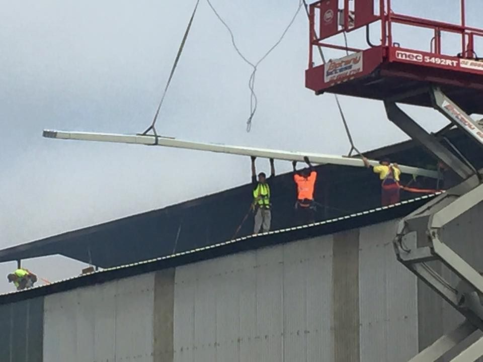 A man is standing on the roof of a building — Kimick Roofing Solutions In Wyong, NSW