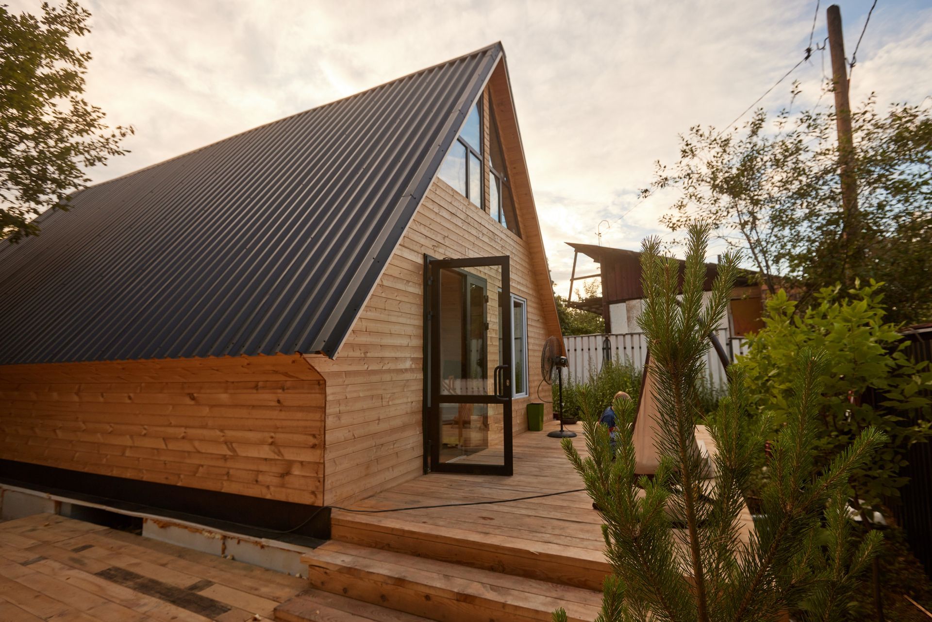 A small wooden house with a black roof is surrounded by trees.