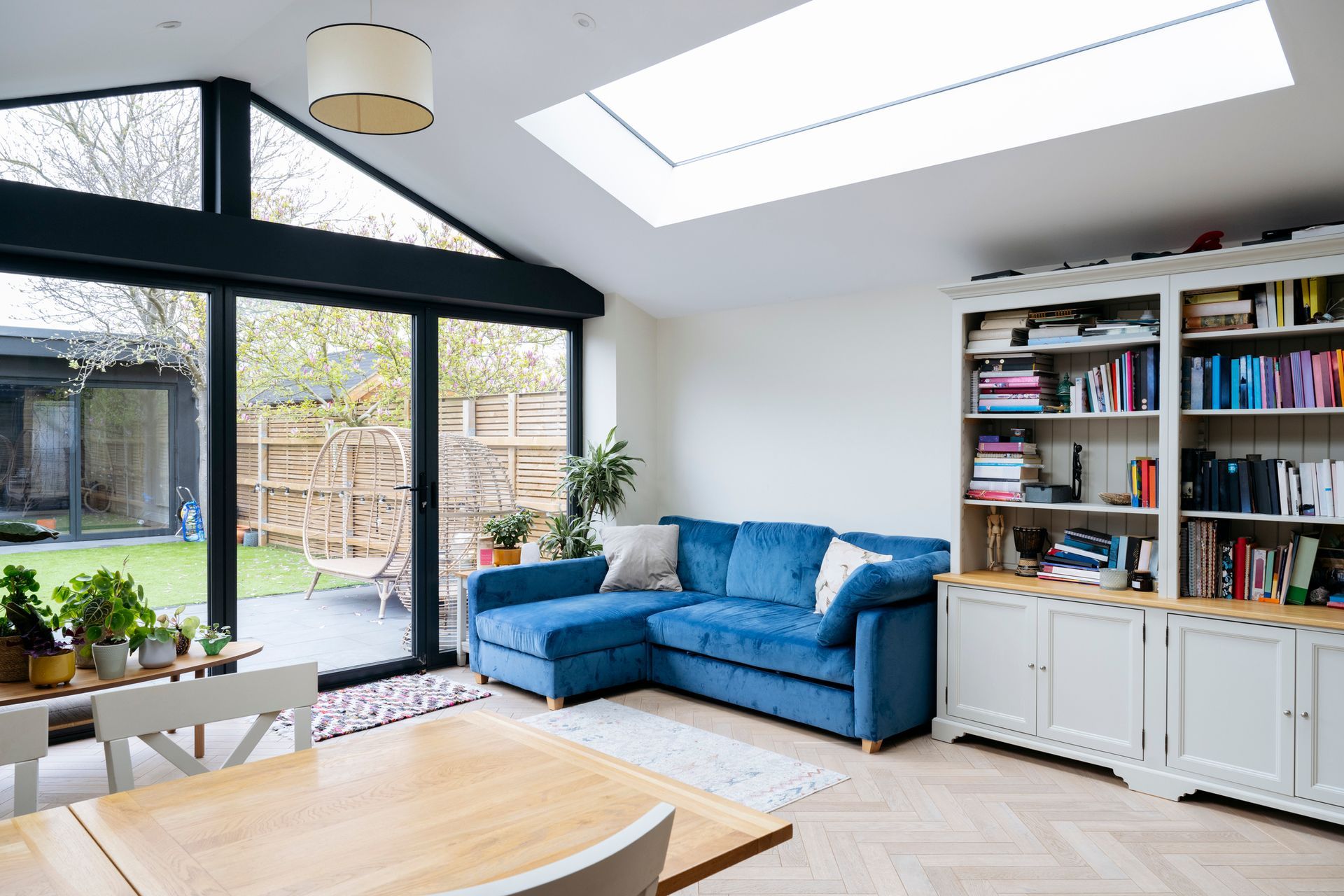 A living room with a blue couch , a dining table , and a skylight.