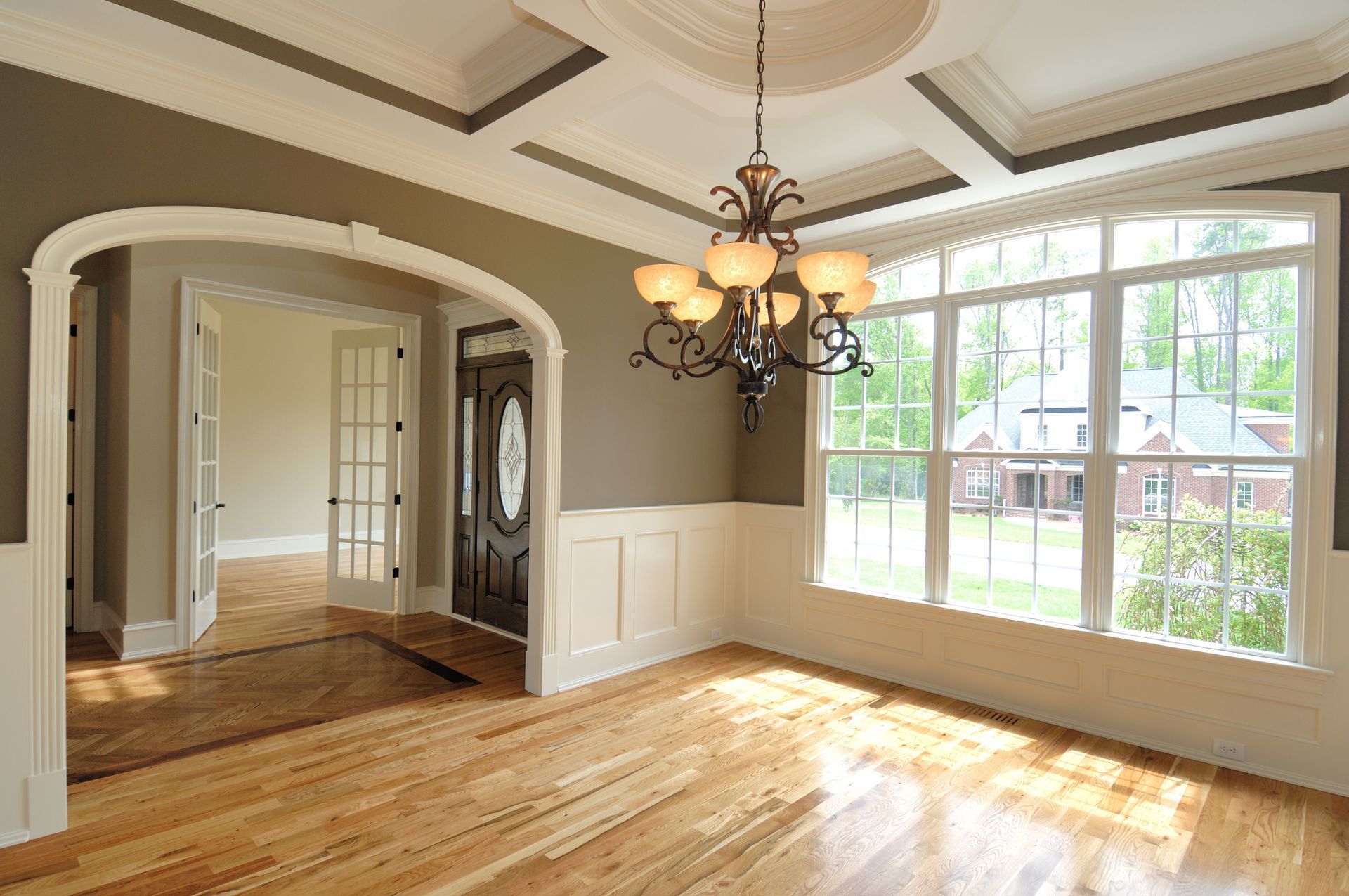 An empty room with hardwood floors and a chandelier hanging from the ceiling.