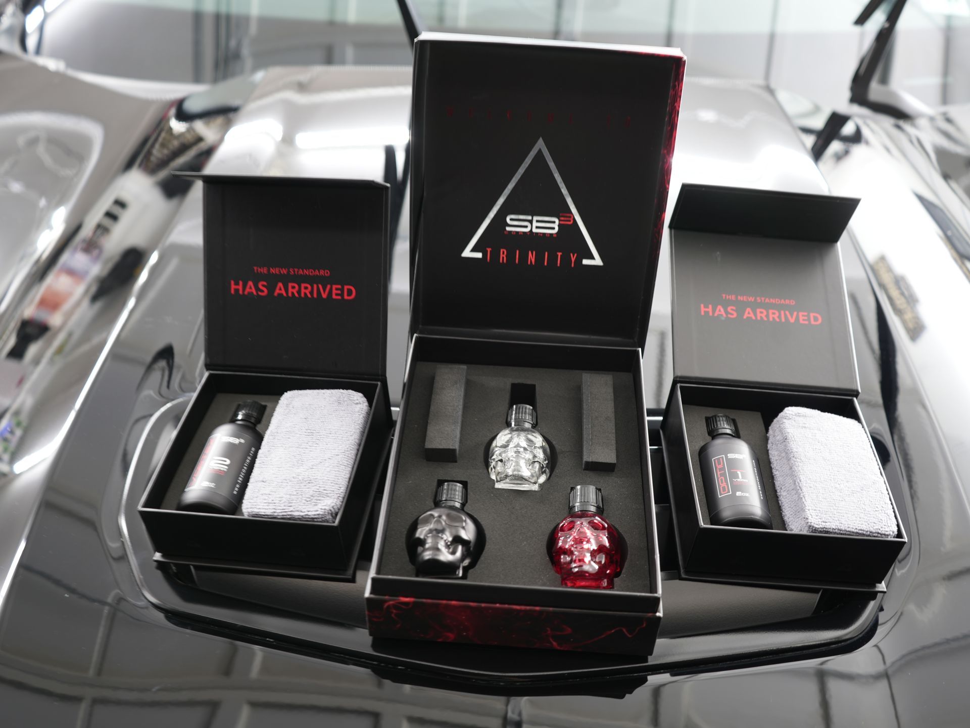 Three boxes of perfume sit on the hood of a car