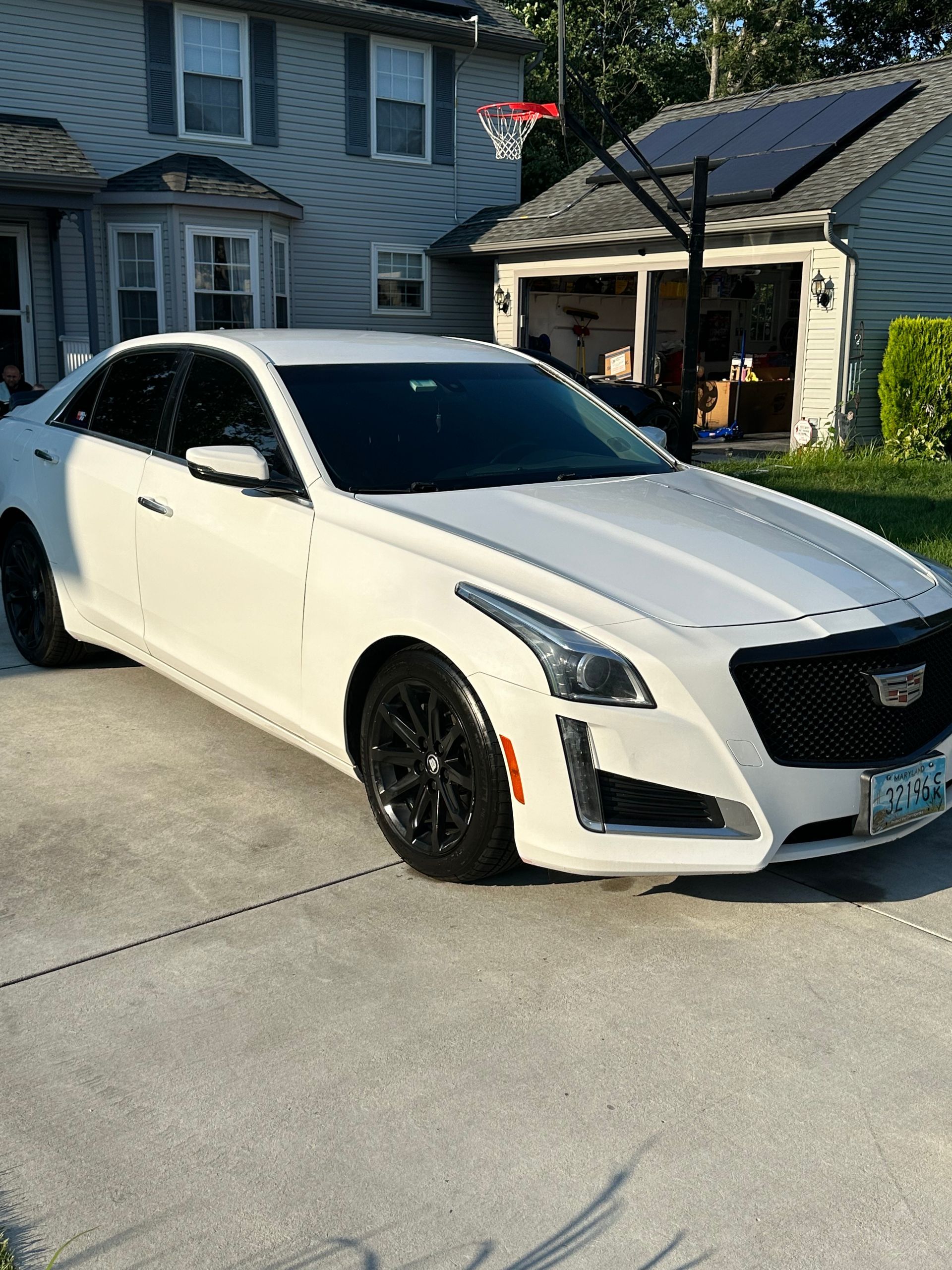 A white cadillac is parked in a driveway in front of a house.