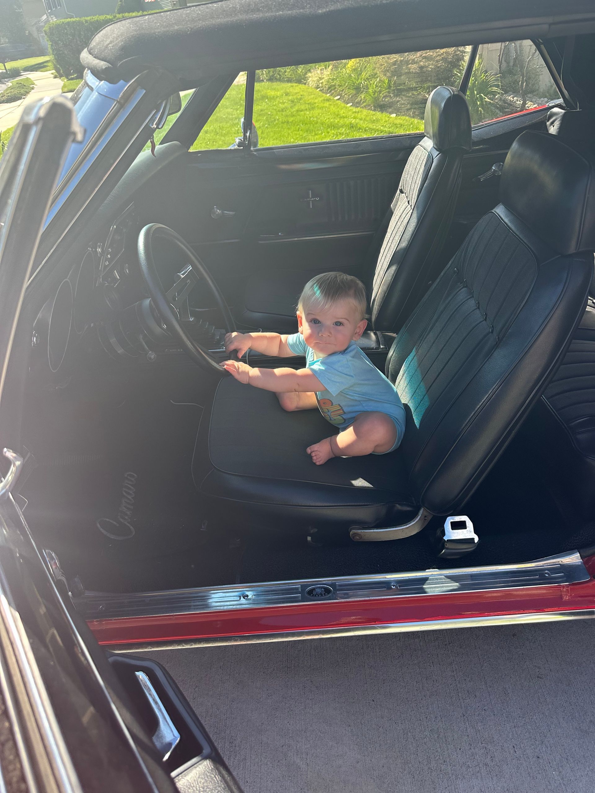 a baby is sitting in the driver 's seat of a red camaro