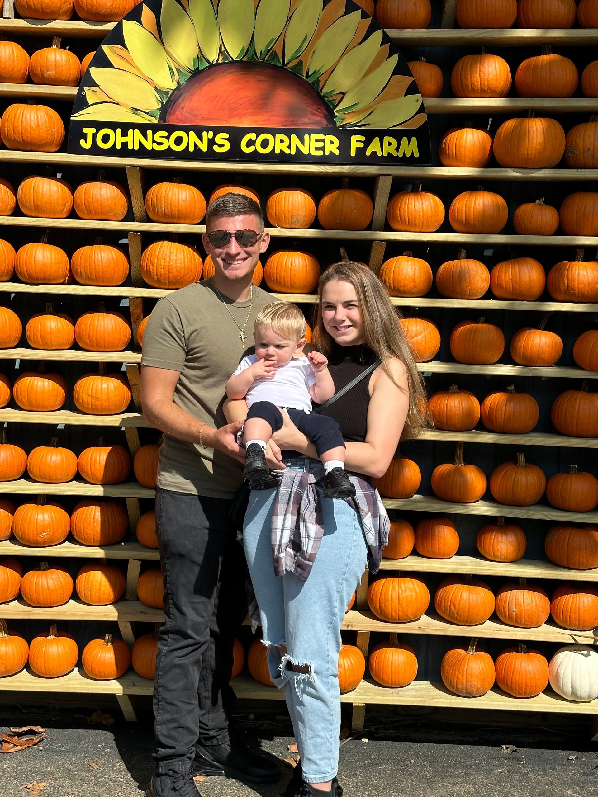 a family poses in front of a wall of pumpkins at johnson 's corner farm