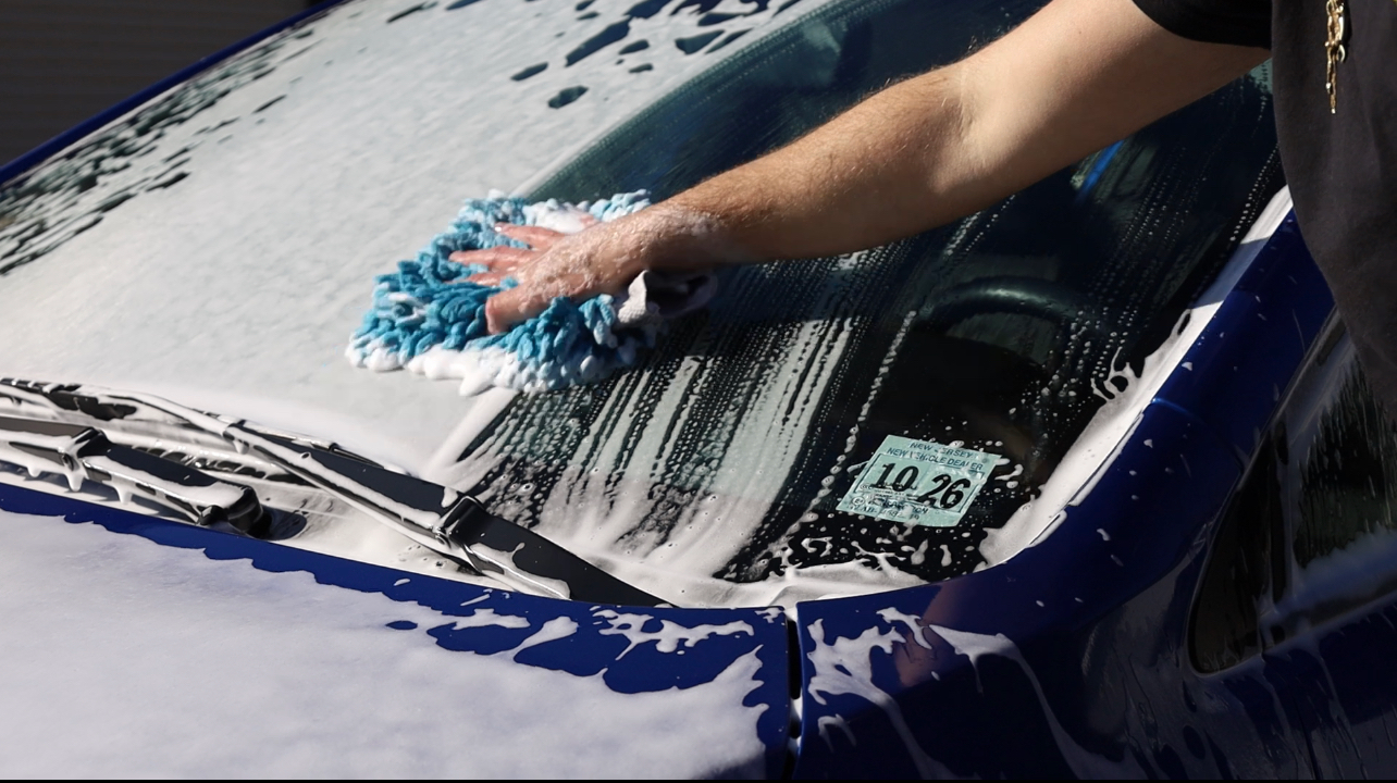 A person is washing the windshield of a blue car