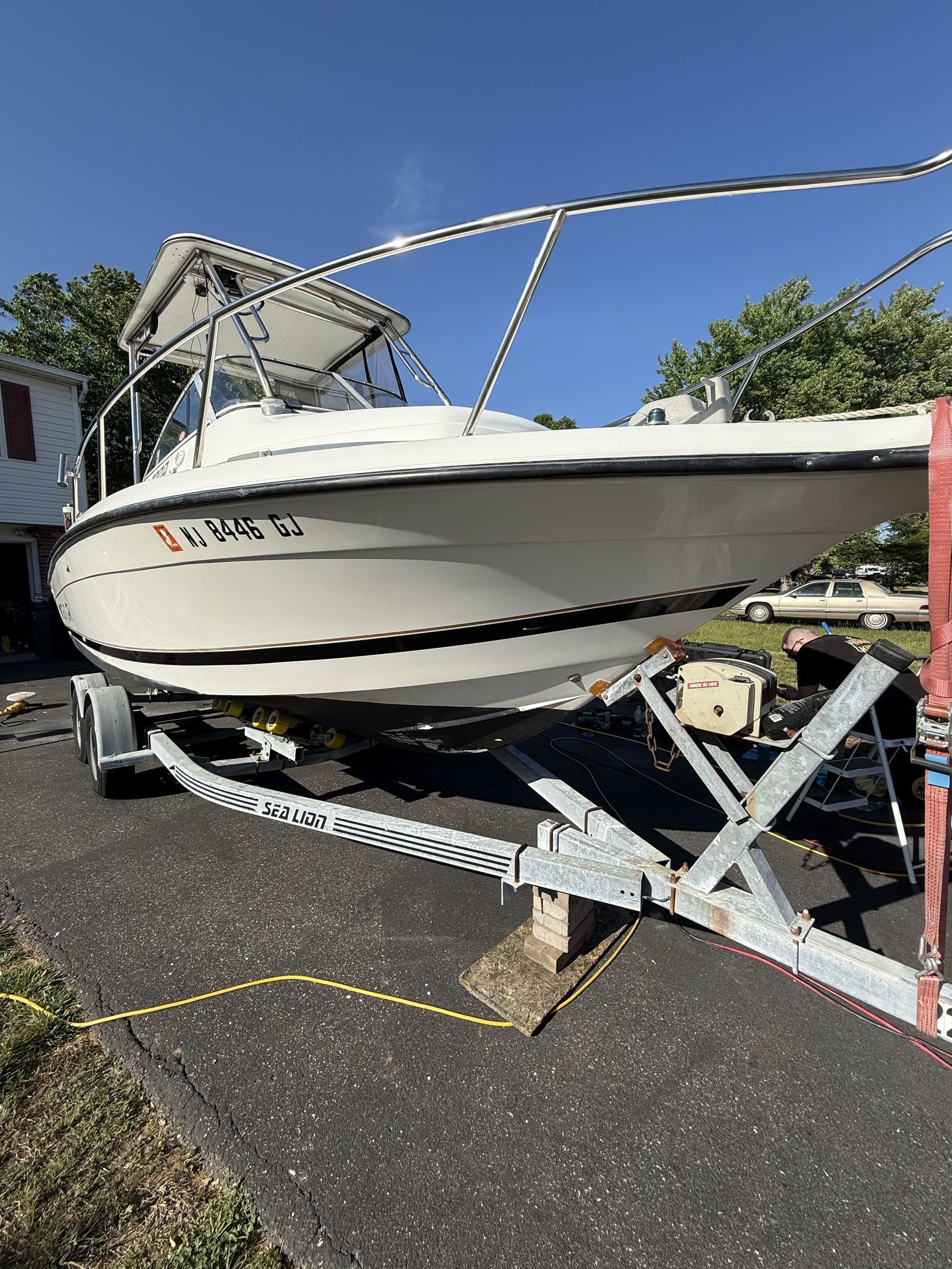 A white boat is parked on a trailer on the side of the road.