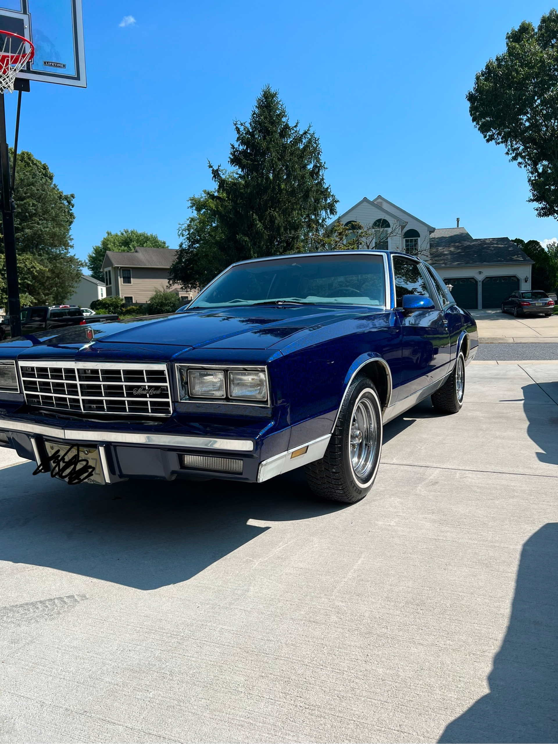 A blue car is parked in front of a basketball hoop.