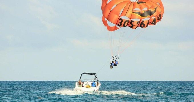 people parasailing with orange parasail over ocean