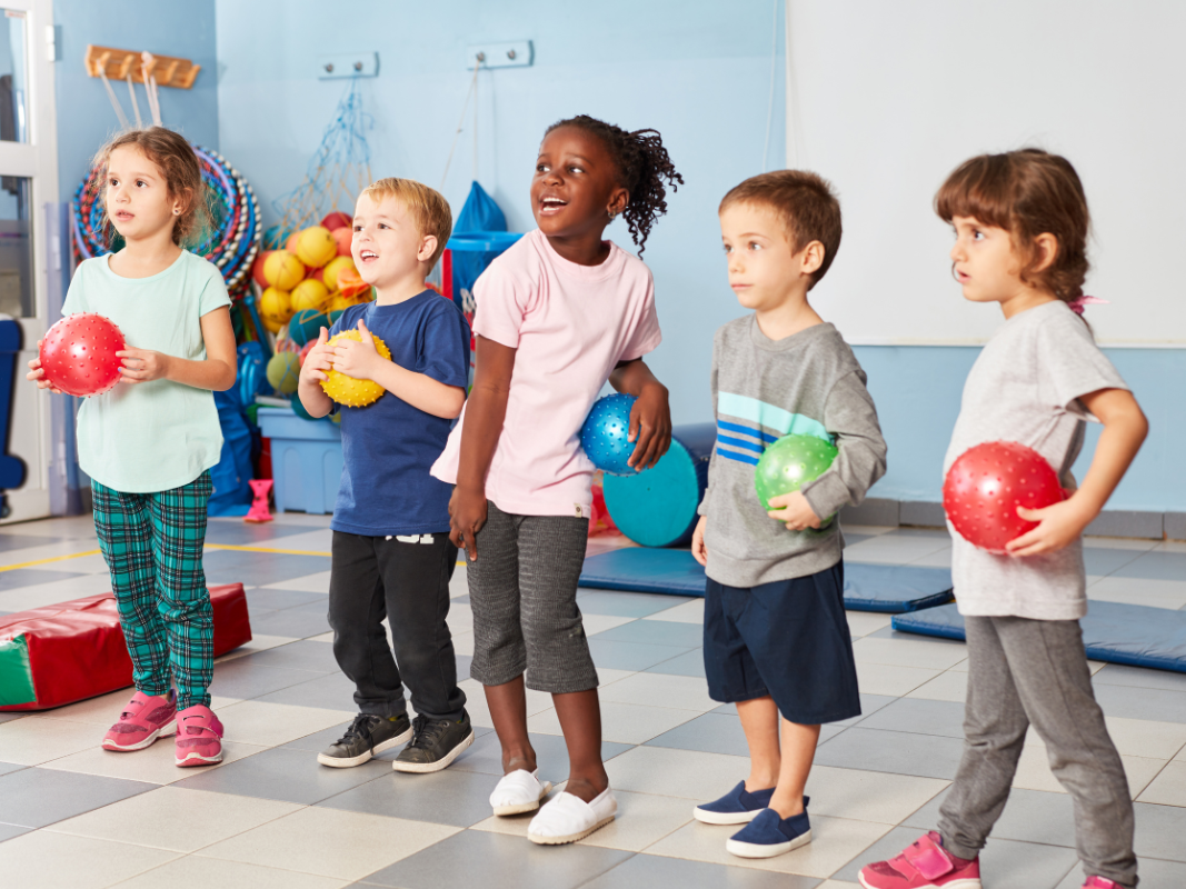 A group of children are holding balls in a gym.