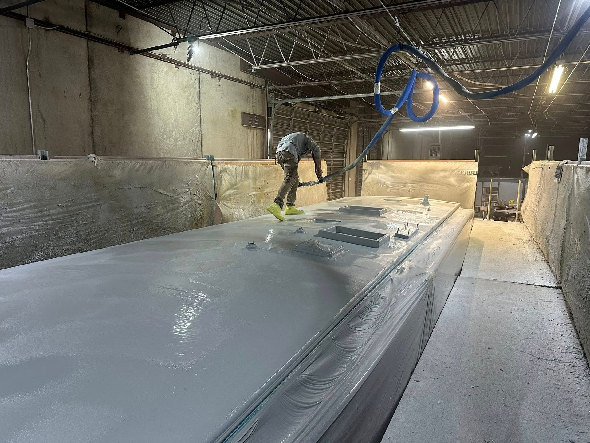 Person spraying a large, flat surface with grey coating in an industrial facility.