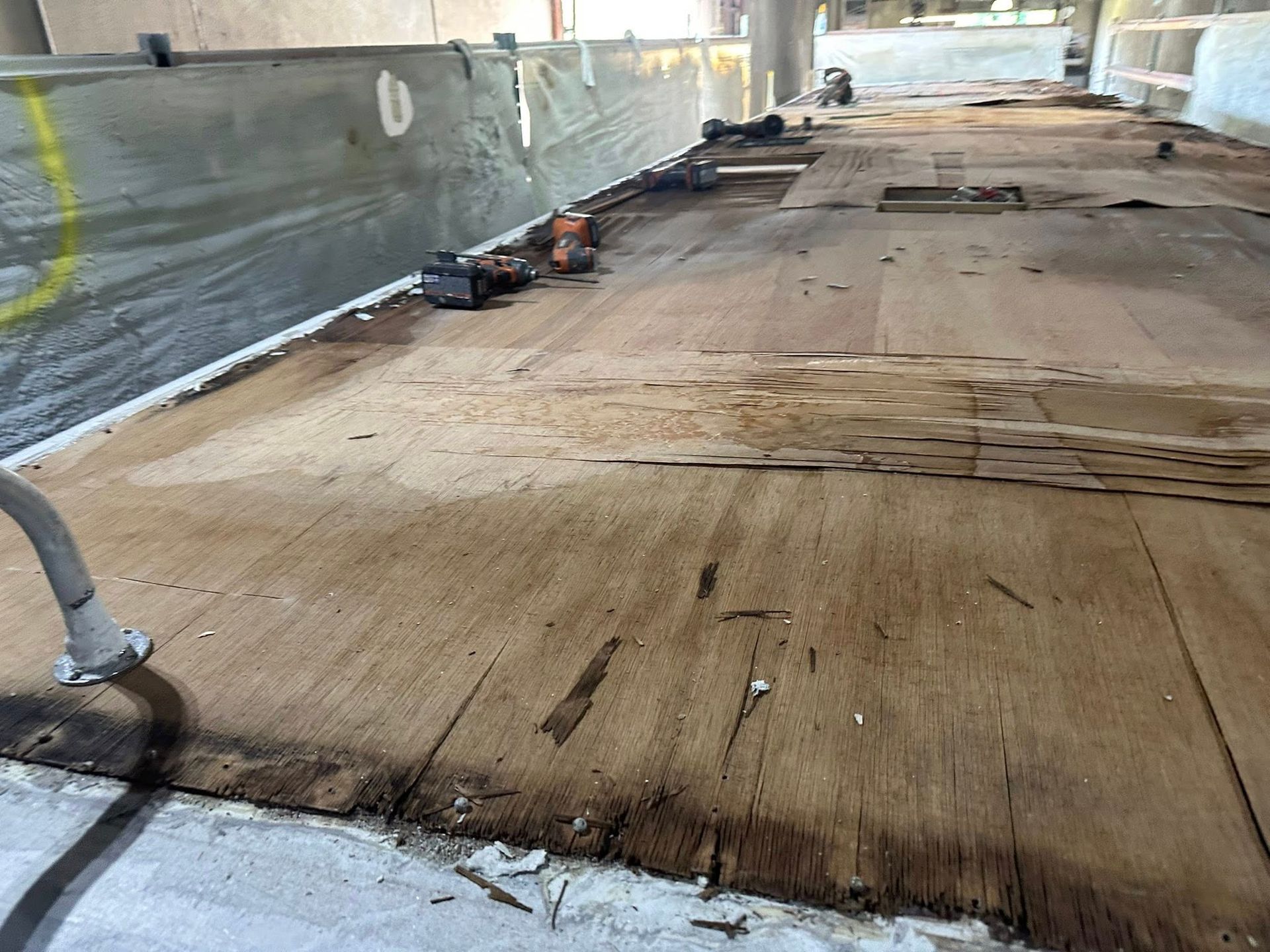 Wooden surface in disrepair, possibly a floor, near a concrete structure. Some tools are present.