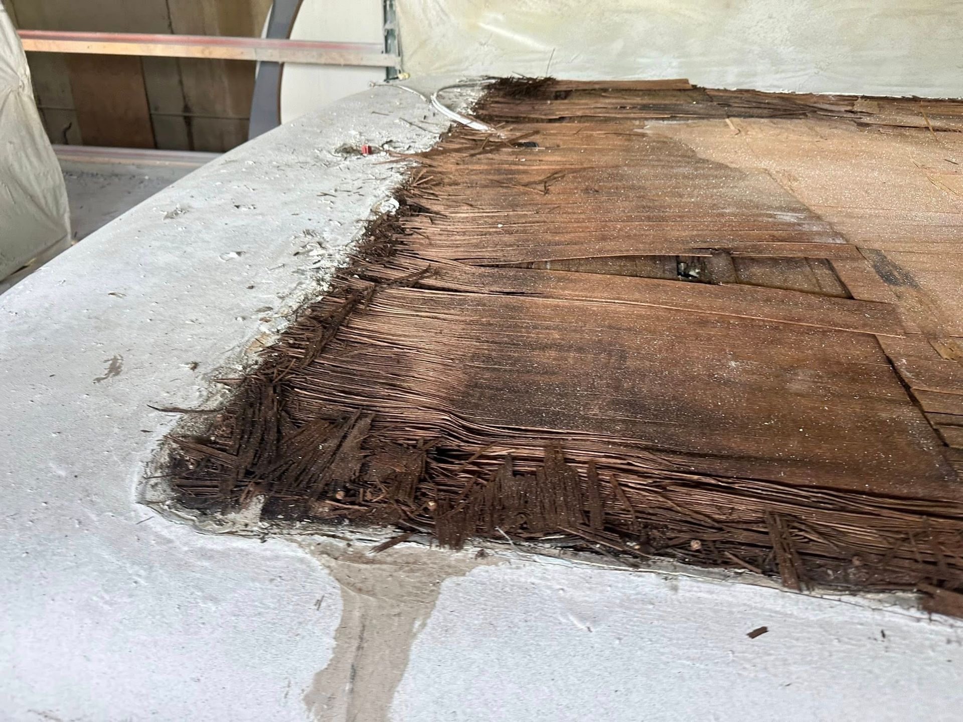 Decayed wood on a concrete surface, likely roof damage. Dark brown wood, gray concrete.