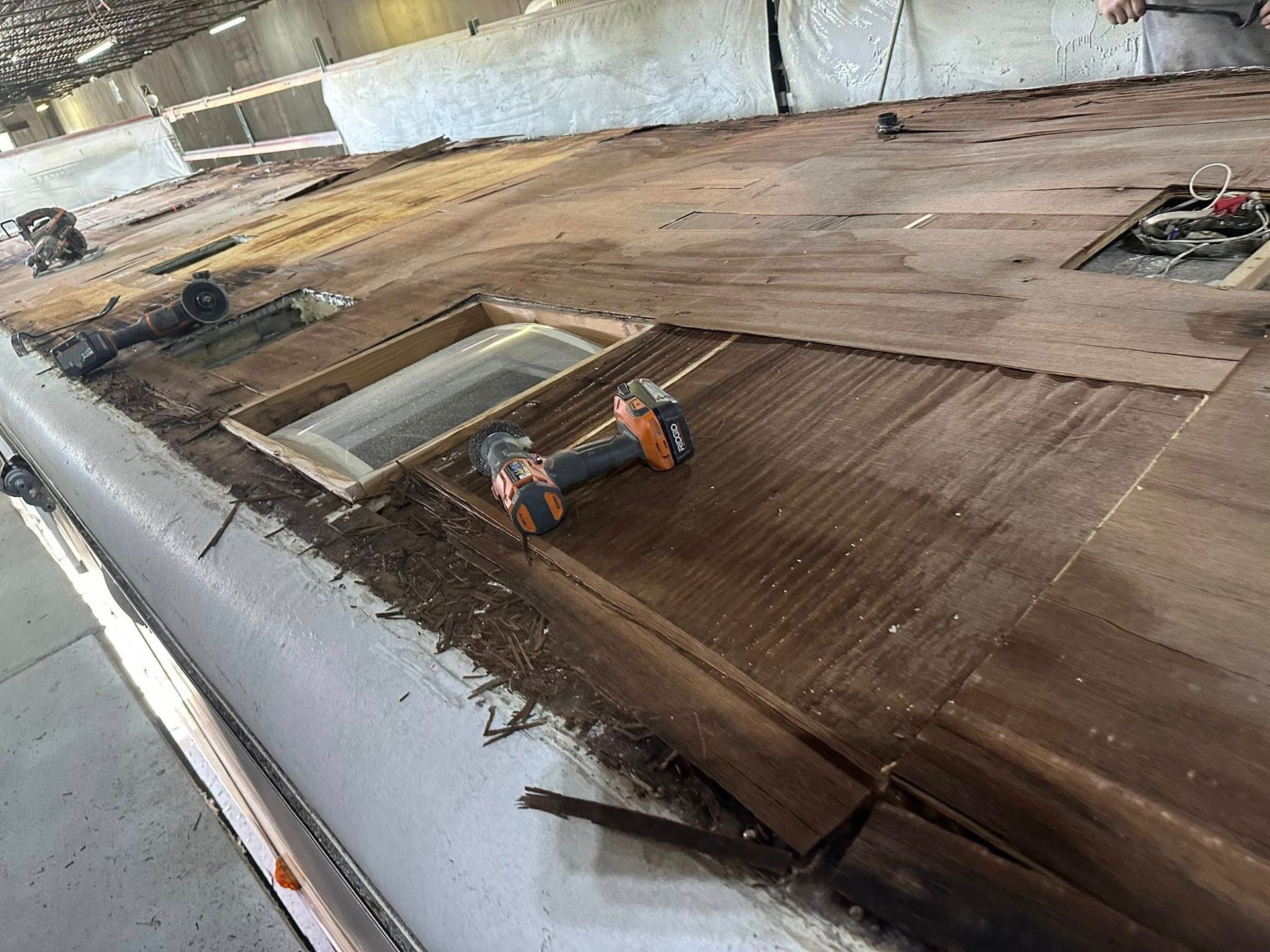 RV roof repair in progress with exposed wood, tools, and a skylight.
