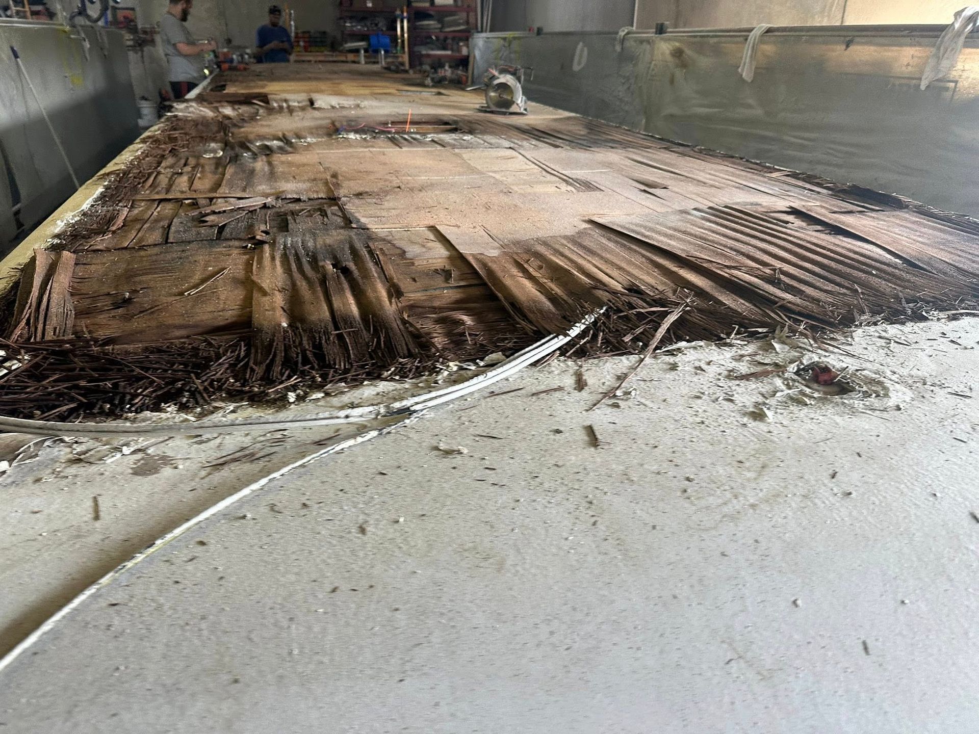 Decaying wood flooring inside a building. A person is visible in the background. White cable in the foreground.