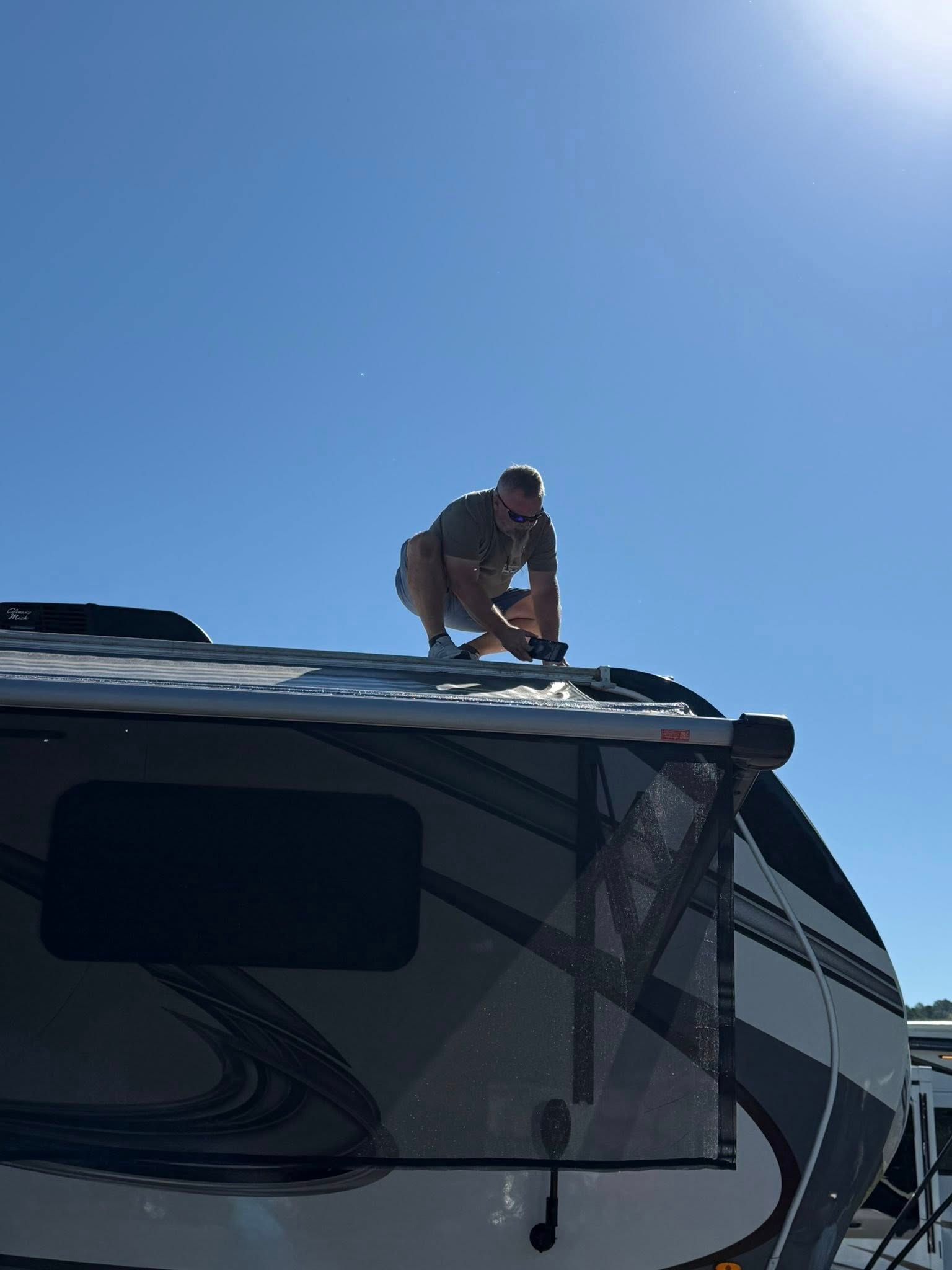 Person on the roof of a recreational vehicle. Sunny, blue sky.