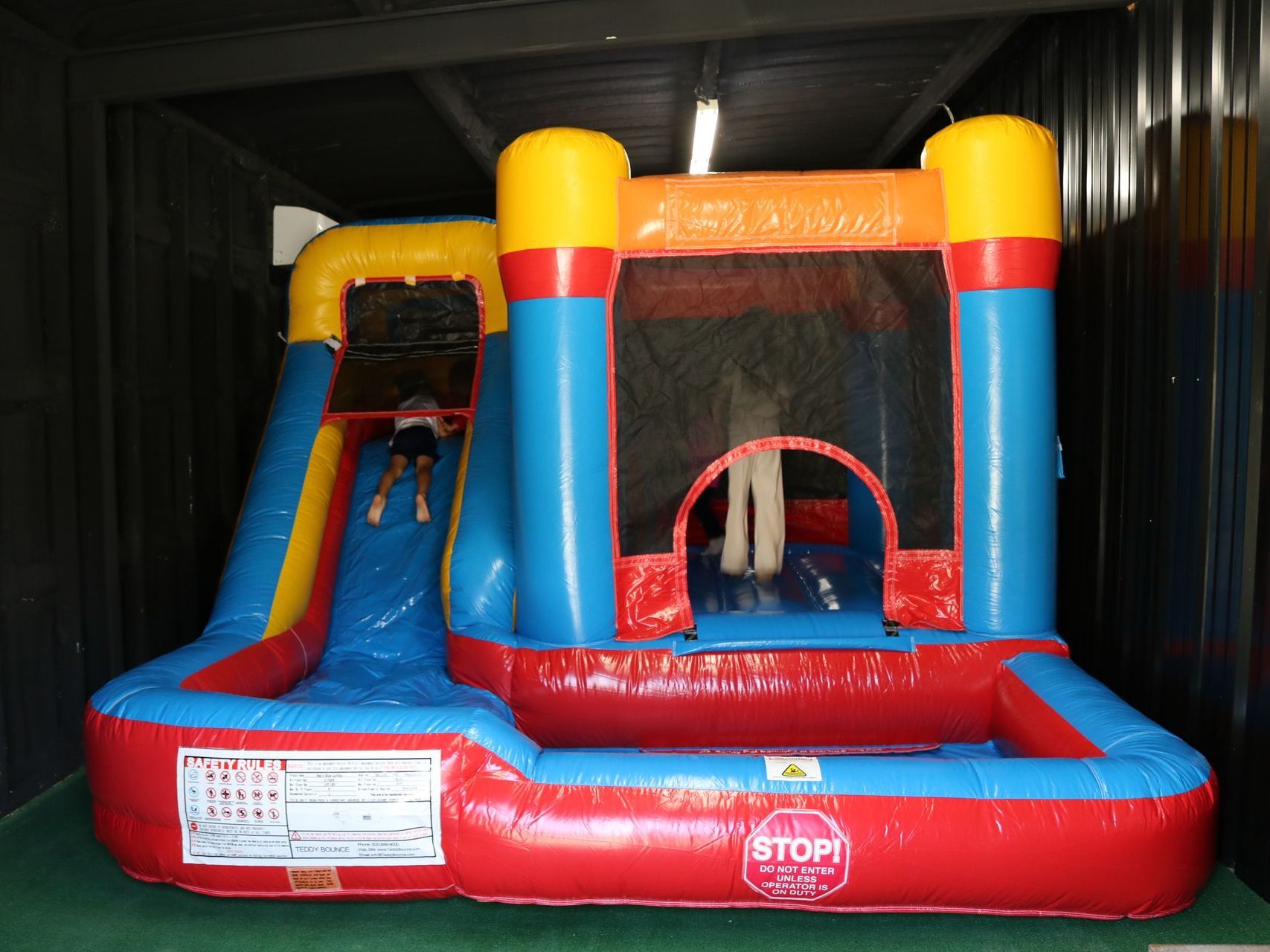 A red , blue and yellow bouncy house with a slide.